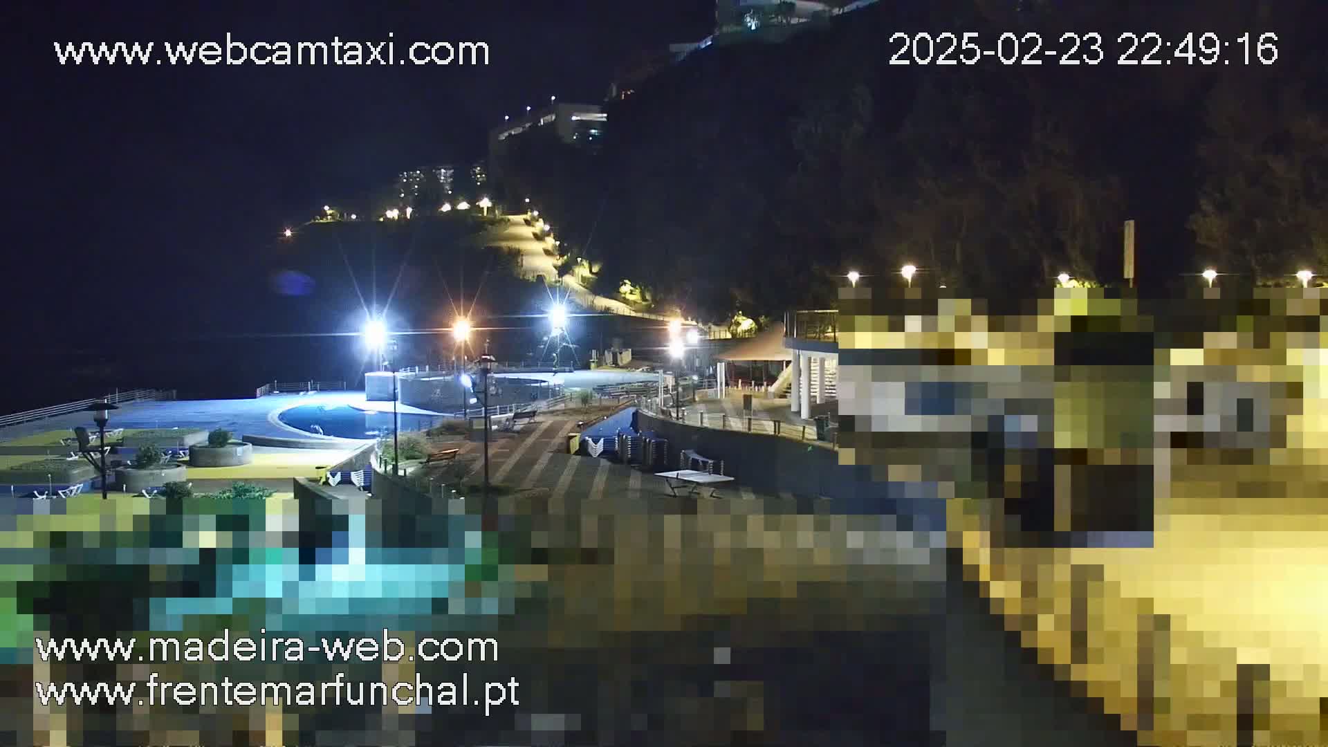A nighttime view of a coastal area with a pool, buildings, and walkways illuminated by lights.