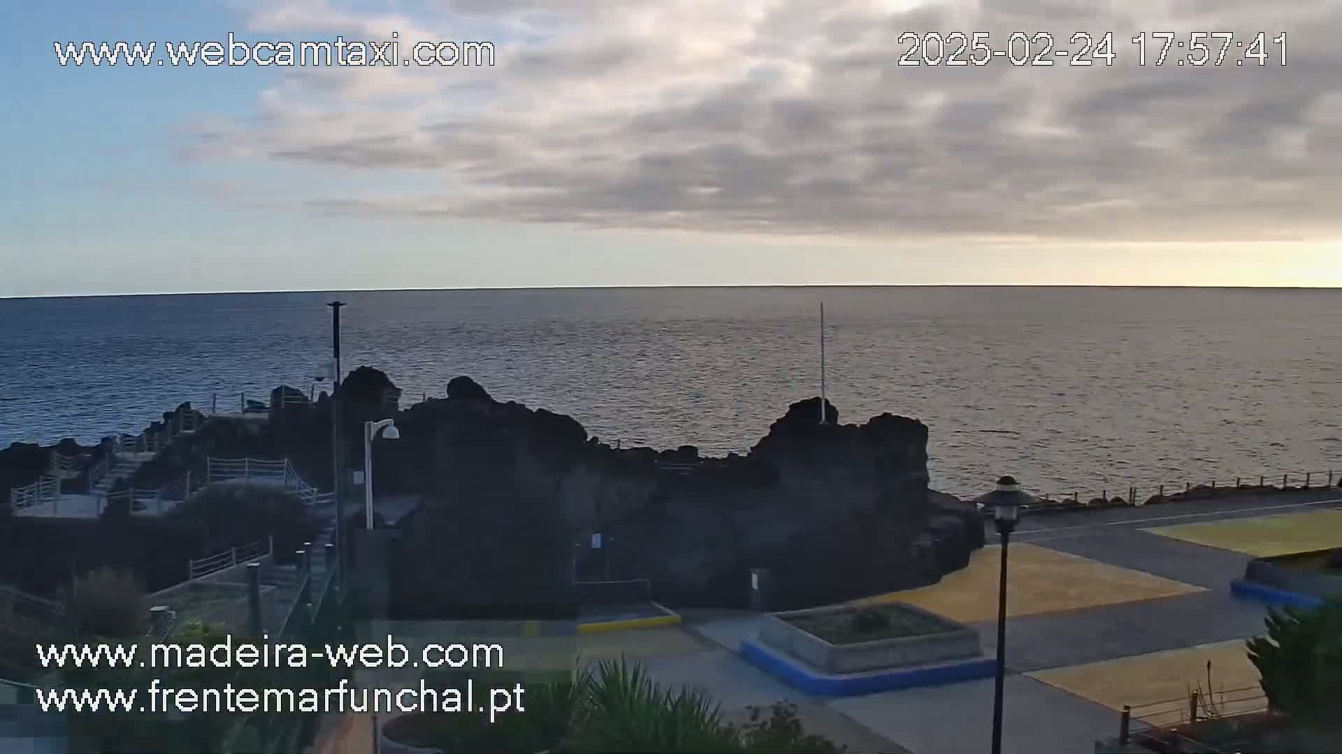 A rocky coastline meets a calm ocean under a mostly cloudy sky.