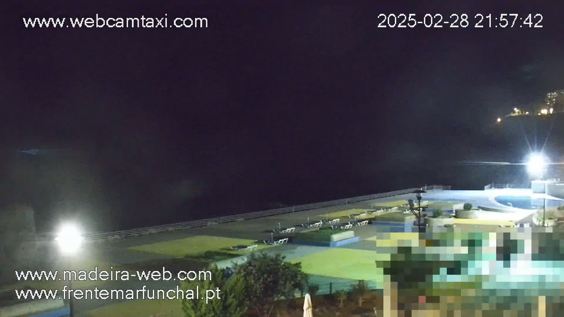 A nighttime view of an outdoor pool area next to a body of water under a dark, clear sky.