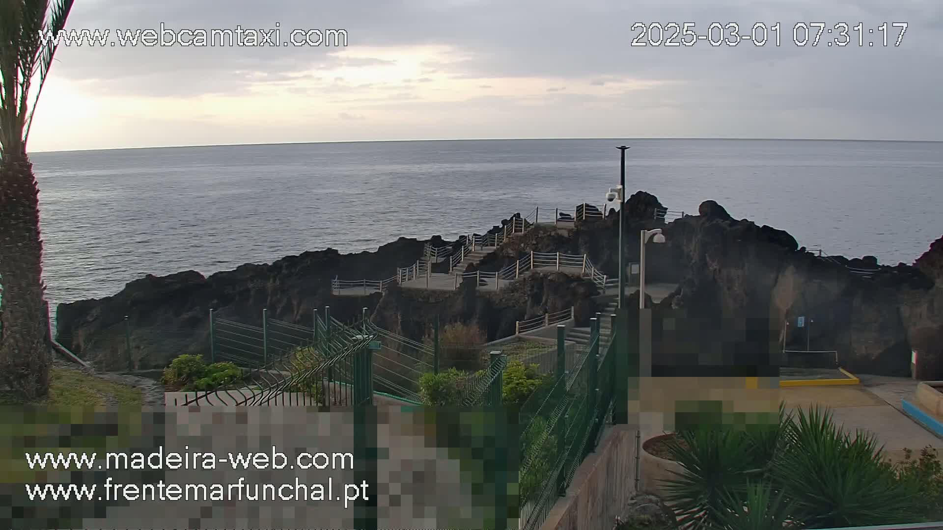 A rocky coastline with stairs and railings leading down to the ocean under an overcast sky.