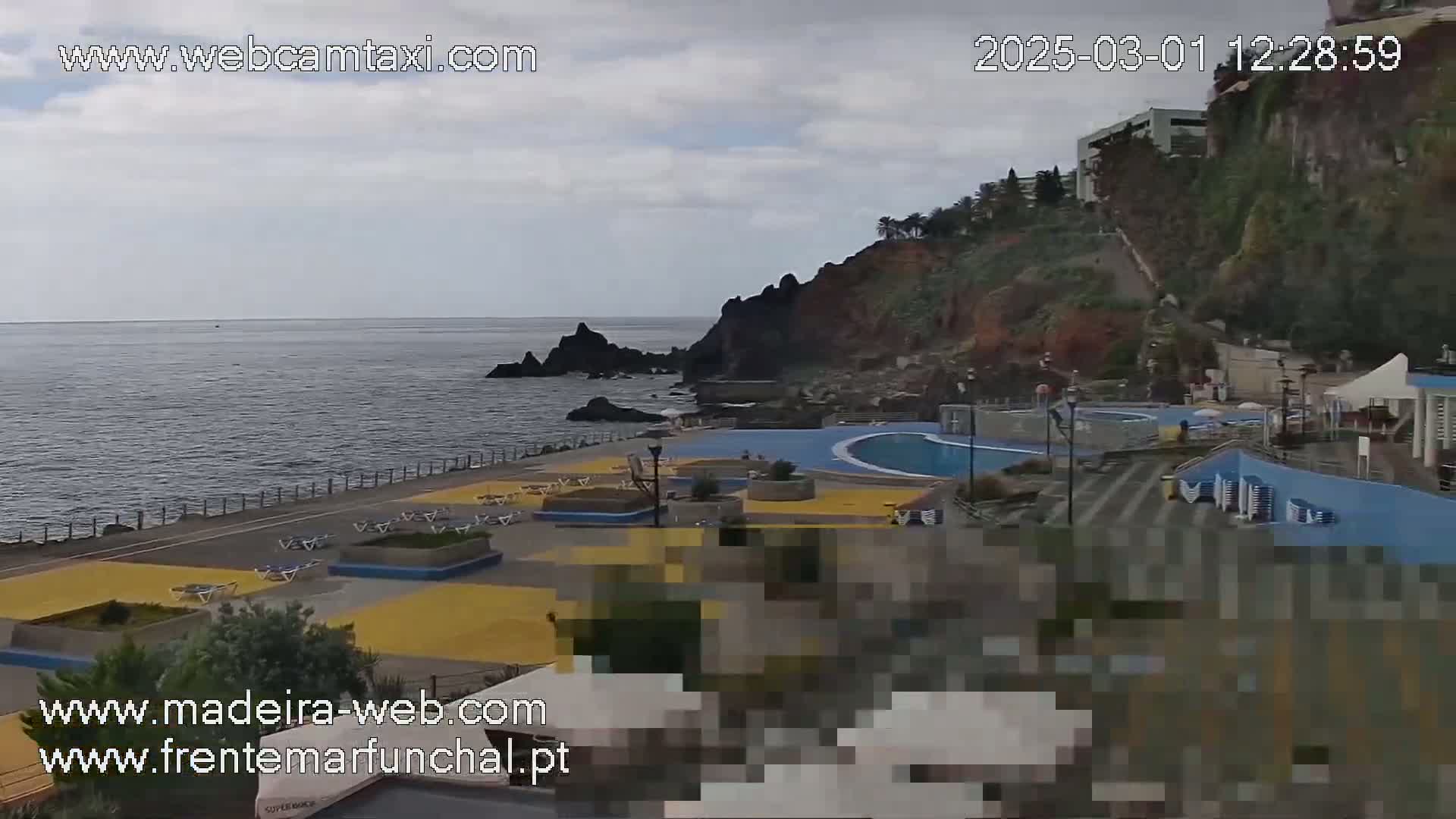 An outdoor scene shows a coastal area with an ocean view, overcast skies, and a pool complex with surrounding deck chairs and landscaping.