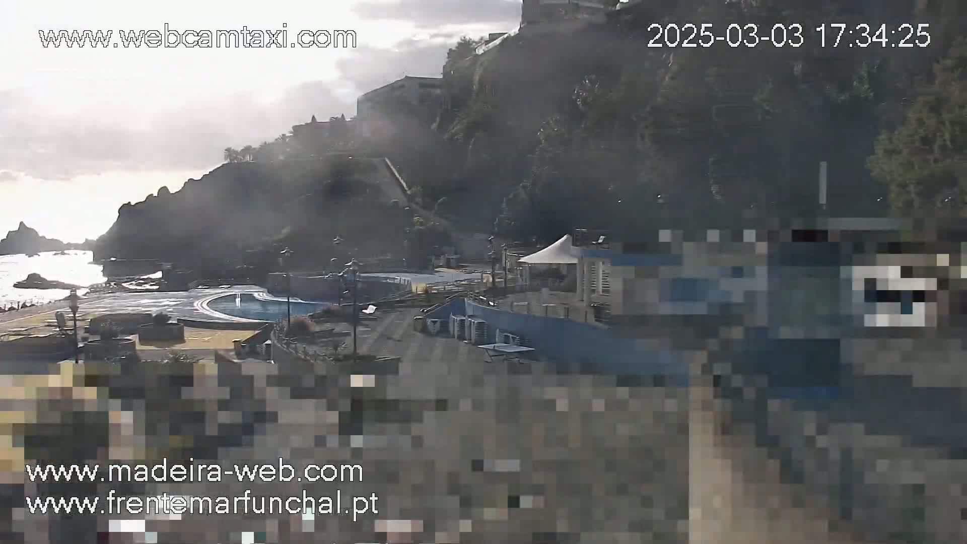 A hazy, overcast day reveals an outdoor scene of a coastal area with buildings, a swimming pool, and rocky cliffs overlooking a calm ocean.