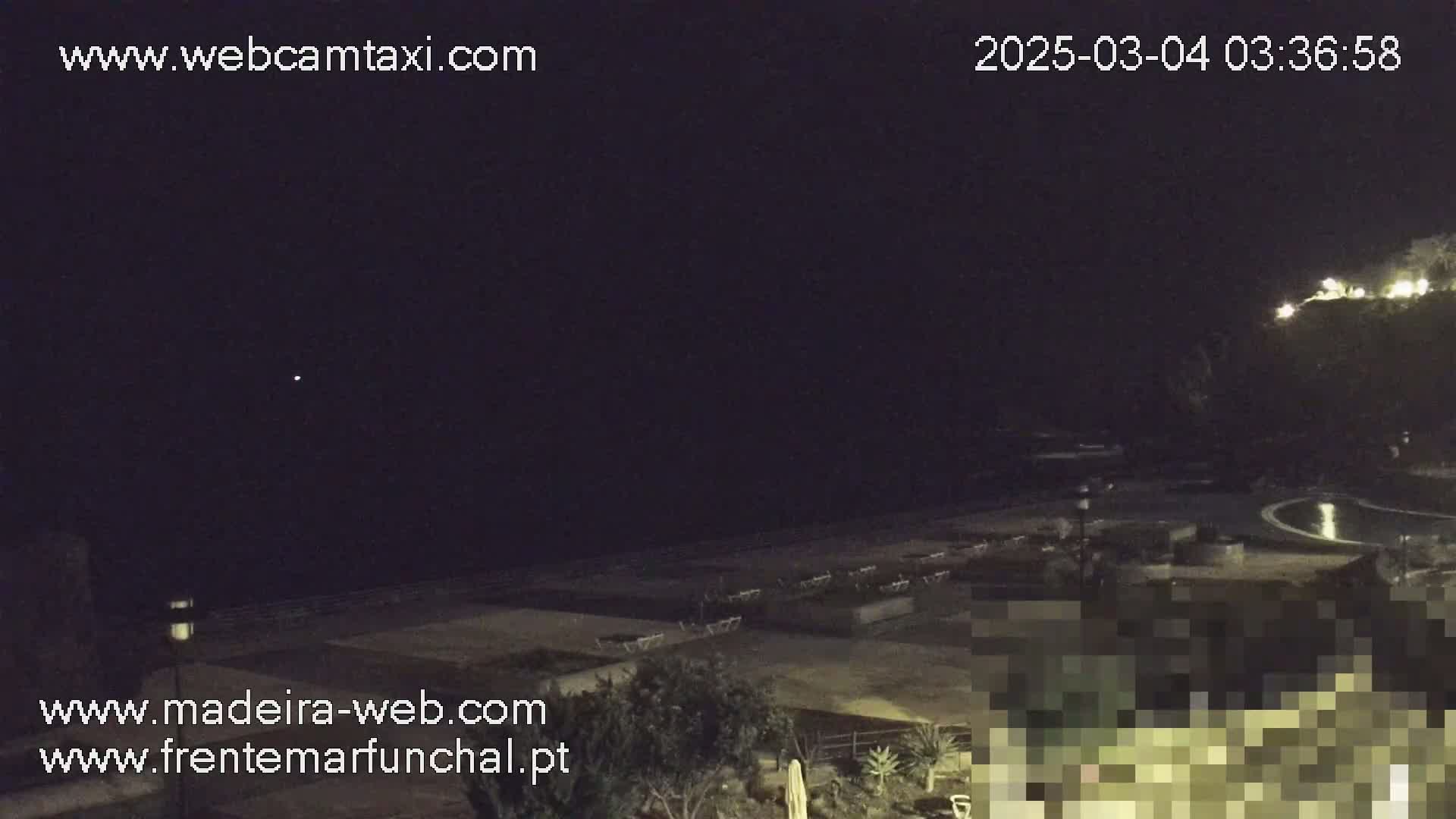 A nighttime view of a dark beach with lounge chairs and a pool, under a clear, dark sky.