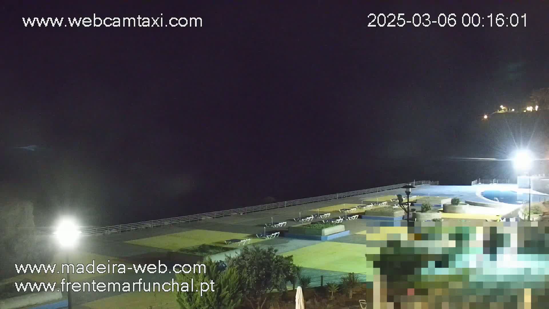 A nighttime view of an outdoor pool area next to a dark ocean under a clear sky.