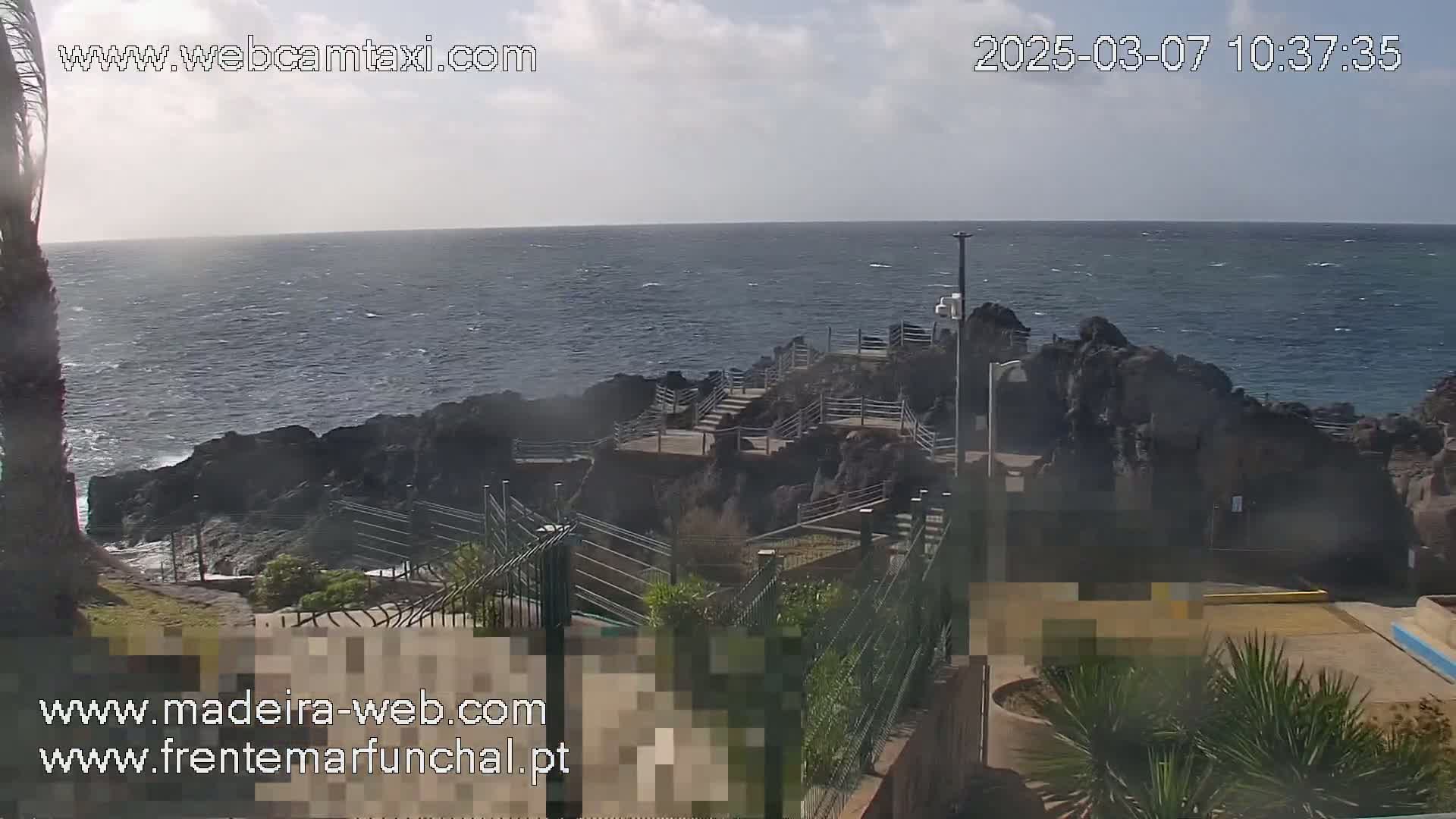 A rocky coastline with a stairway leading down to the ocean under a partly cloudy sky.
