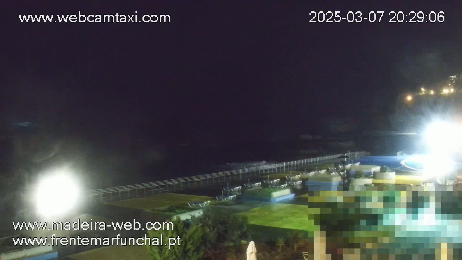 A nighttime view of a coastal area with a pool and patio furniture, under a dark sky.