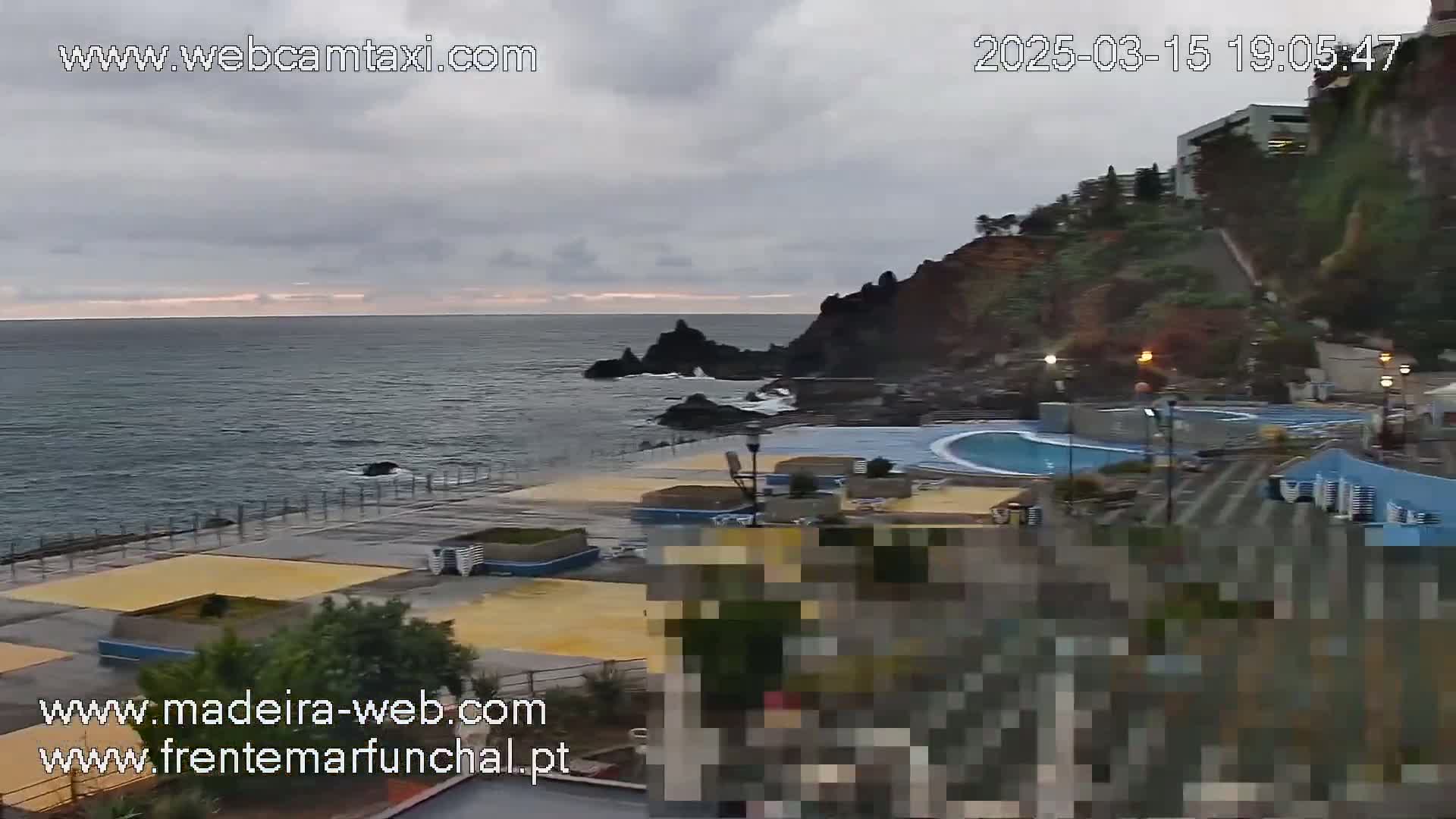 An overcast day reveals a rocky coastline with an oceanside pool area and buildings perched on a cliff.