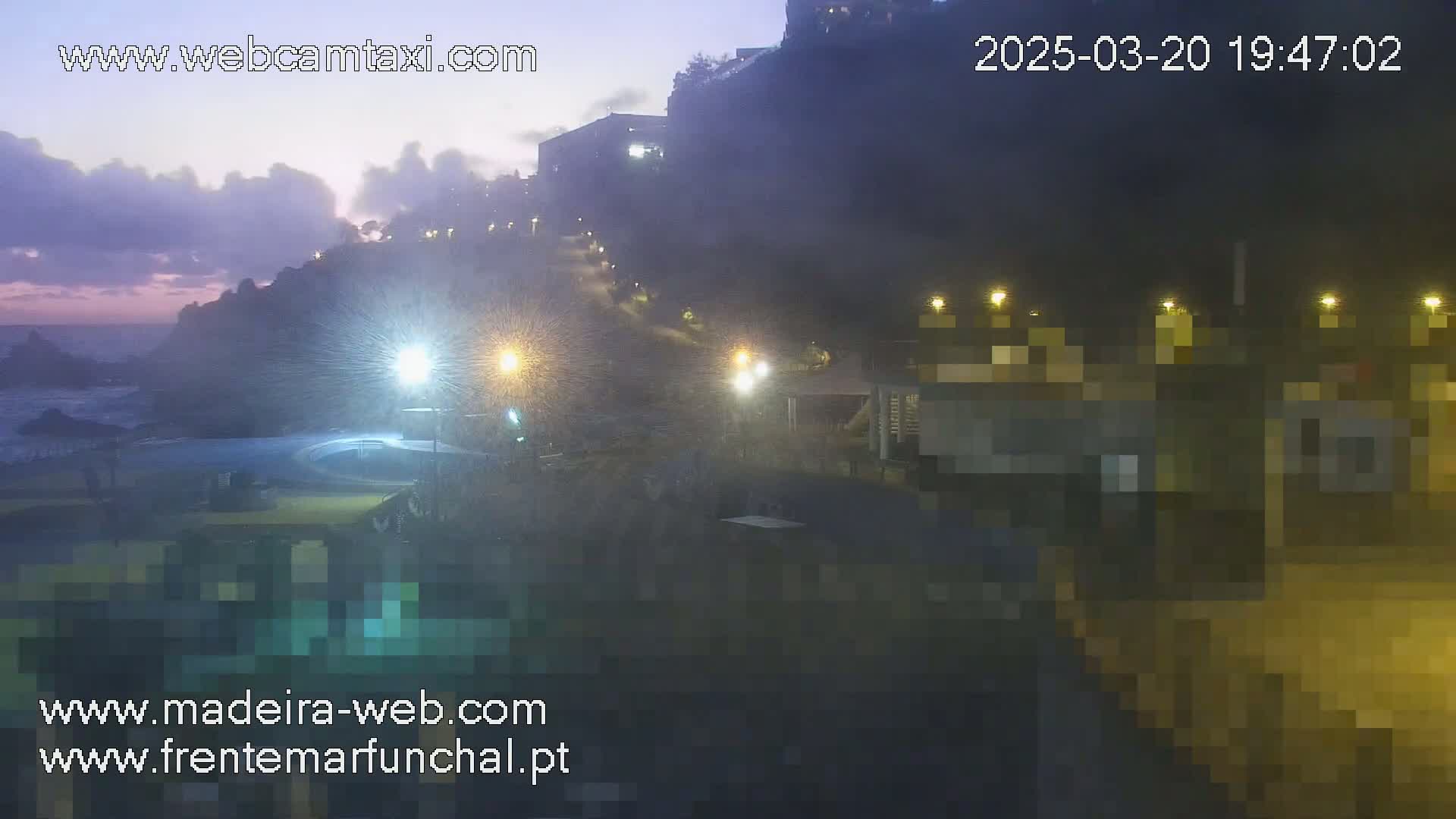 A nighttime coastal scene shows a hazy, dimly lit town built on a cliff overlooking a dark ocean under a dusky sky.