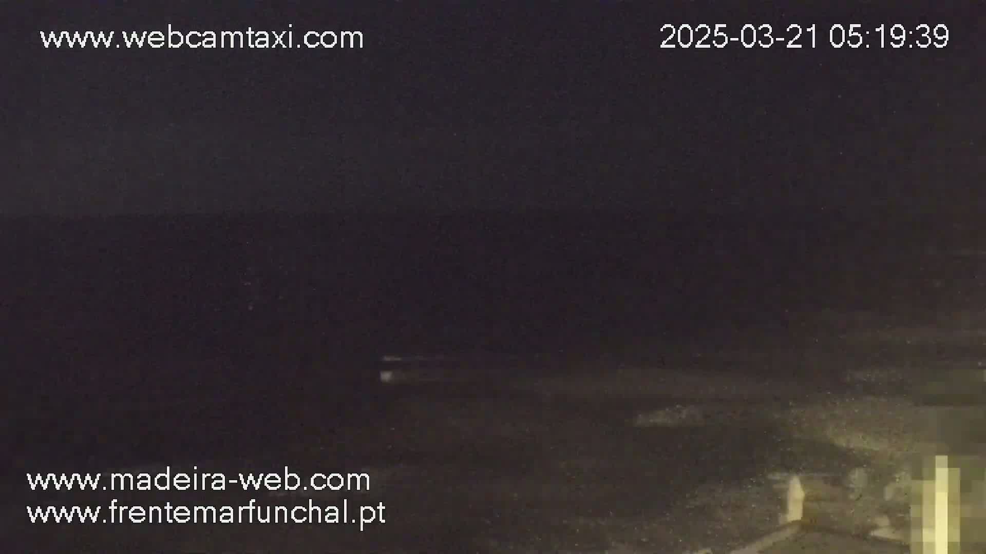 A dark, nighttime view of a shoreline with a slightly visible body of water.