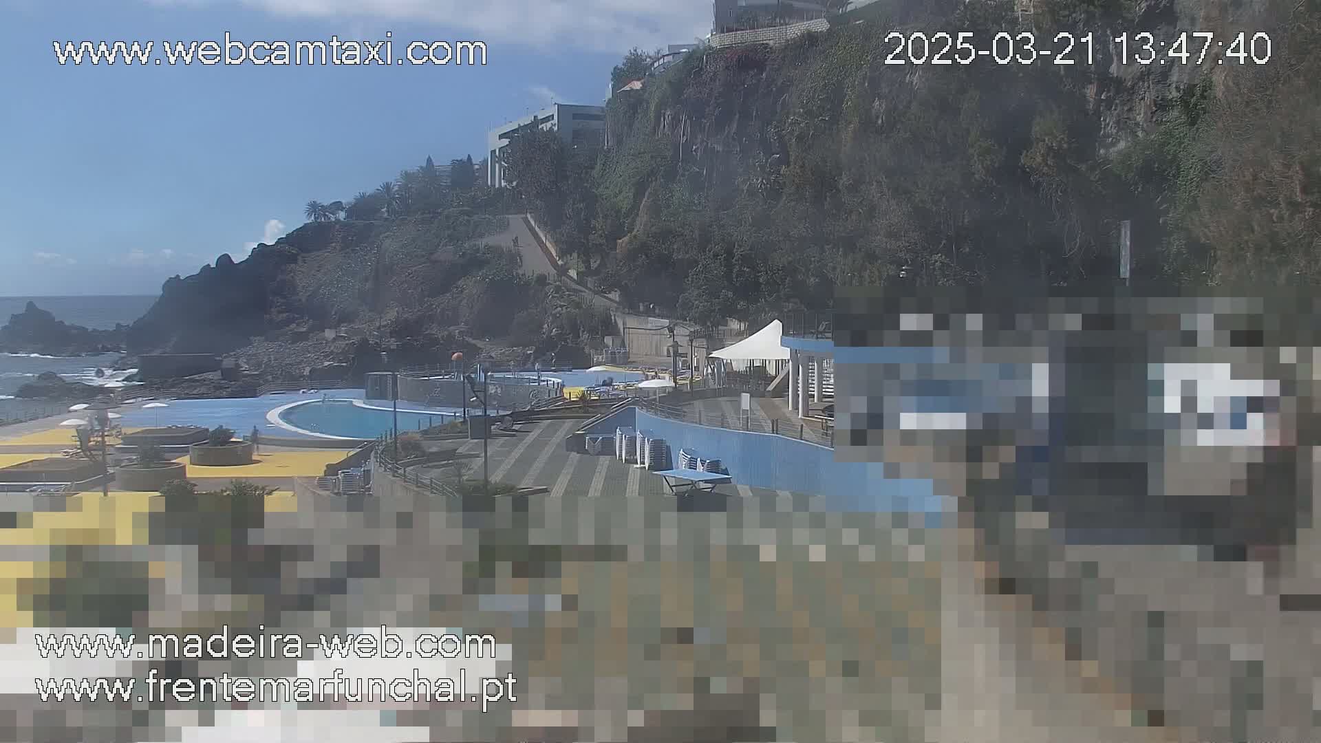 An outdoor view of a seaside pool complex situated on a rocky cliff overlooking the ocean under a clear, sunny sky.