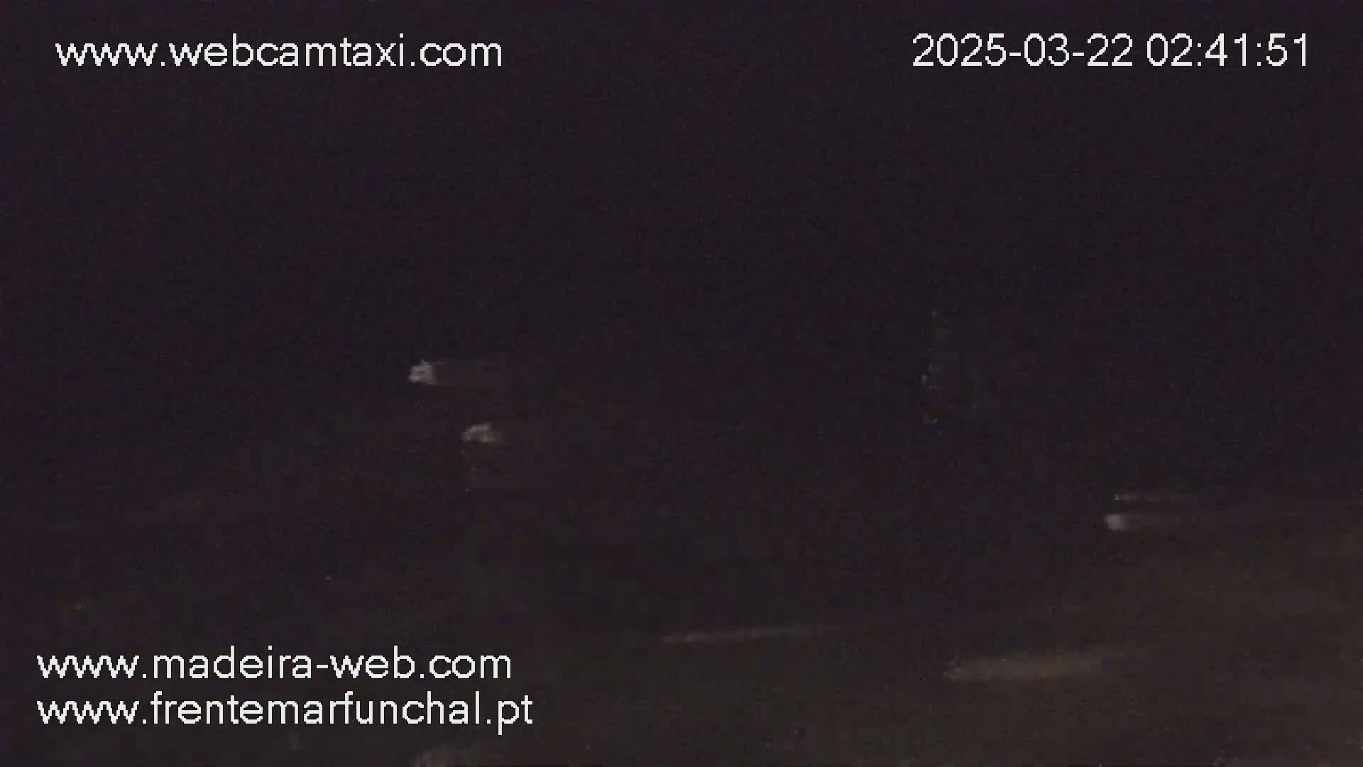 A nighttime, low-light outdoor image shows a dark scene with very faint lights in the distance.