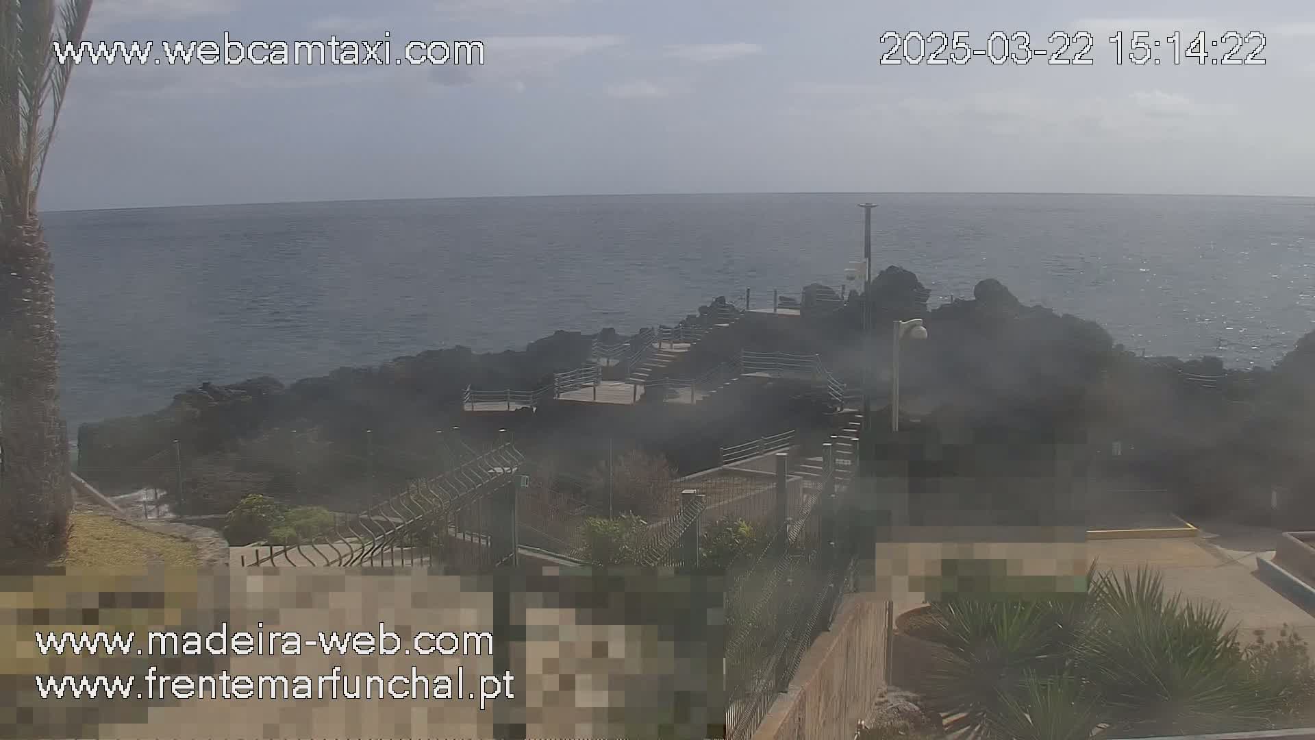 A hazy, sunny day overlooks a rocky coastline with a stairway leading down to the ocean.
