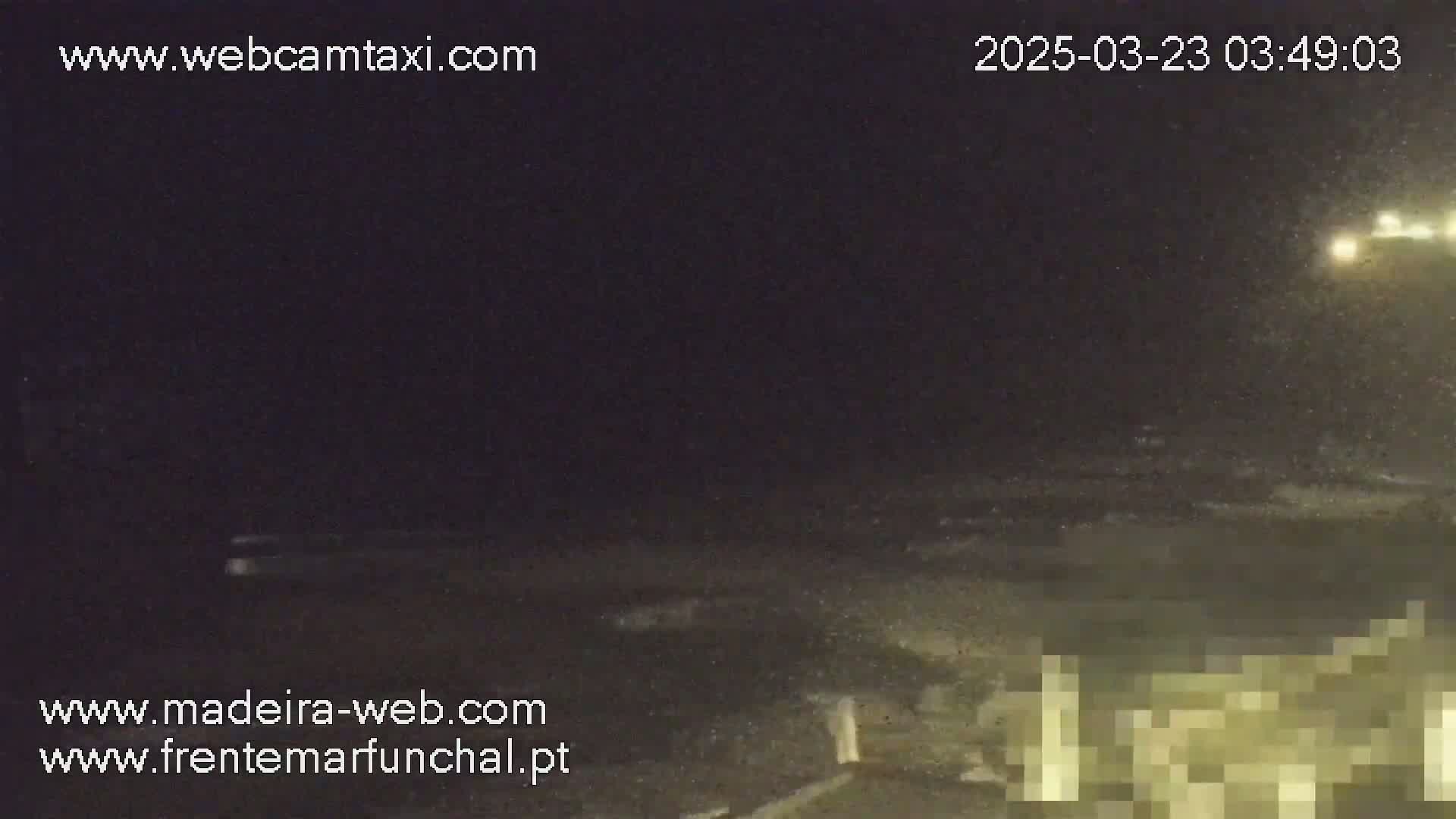 A nighttime, snowy scene shows dark, turbulent water near a shoreline with a blurred, illuminated structure in the lower right corner.