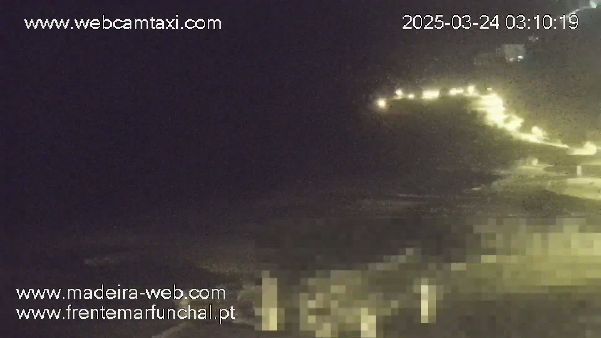 A nighttime coastal scene shows a dark ocean with a dimly lit shoreline featuring buildings and roads.