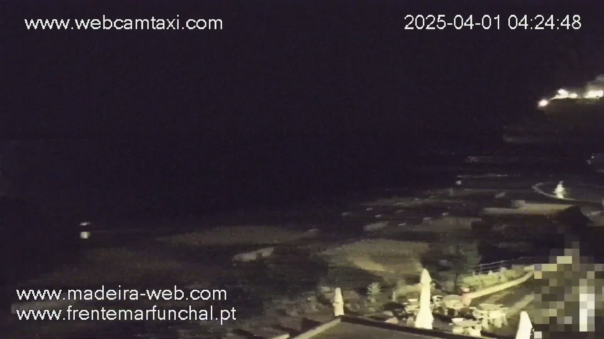A nighttime, dark view of a beach and ocean with some lights visible in the distance.