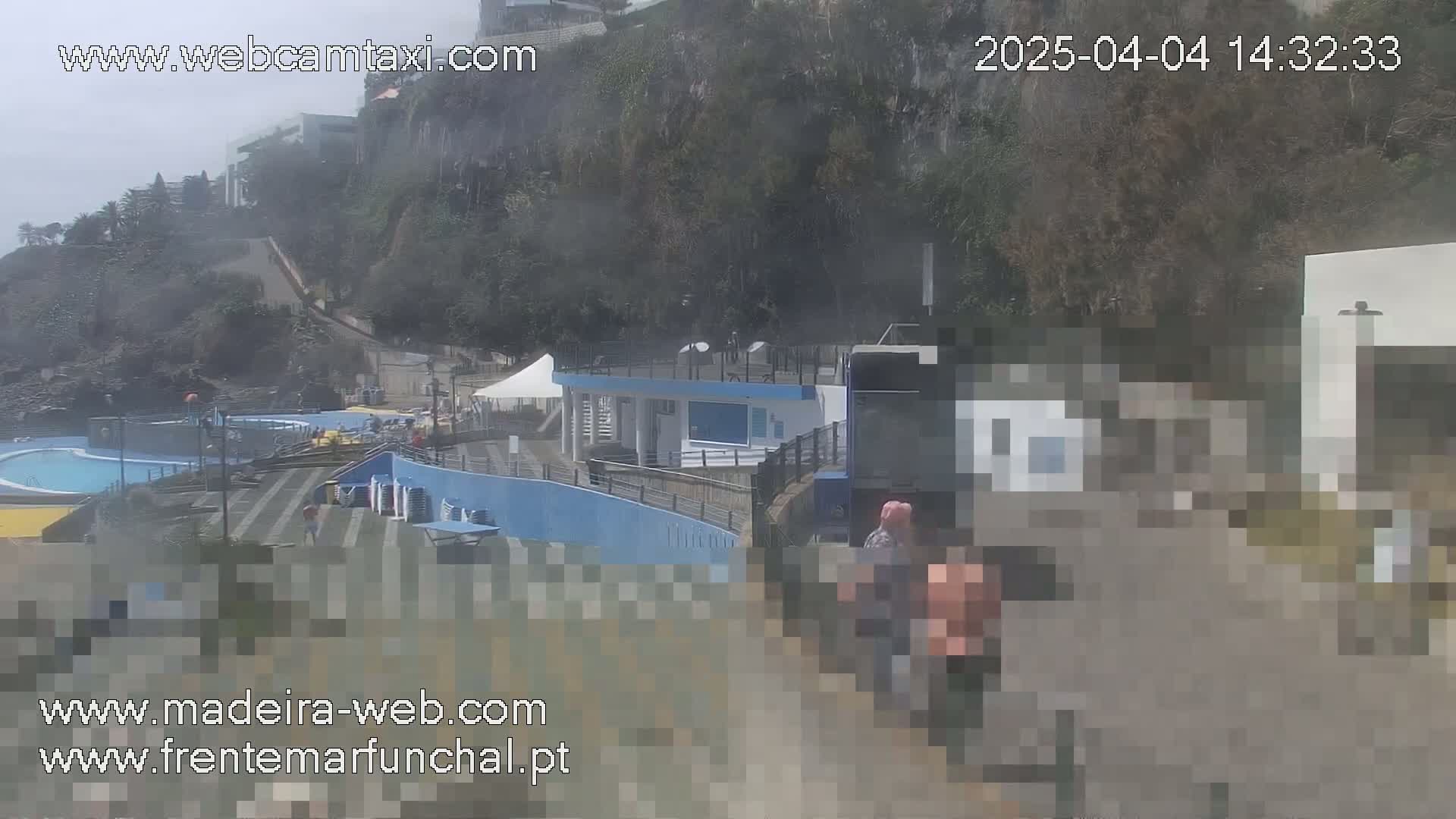 A hazy outdoor scene shows a pool area and buildings near a steep, heavily vegetated hillside.