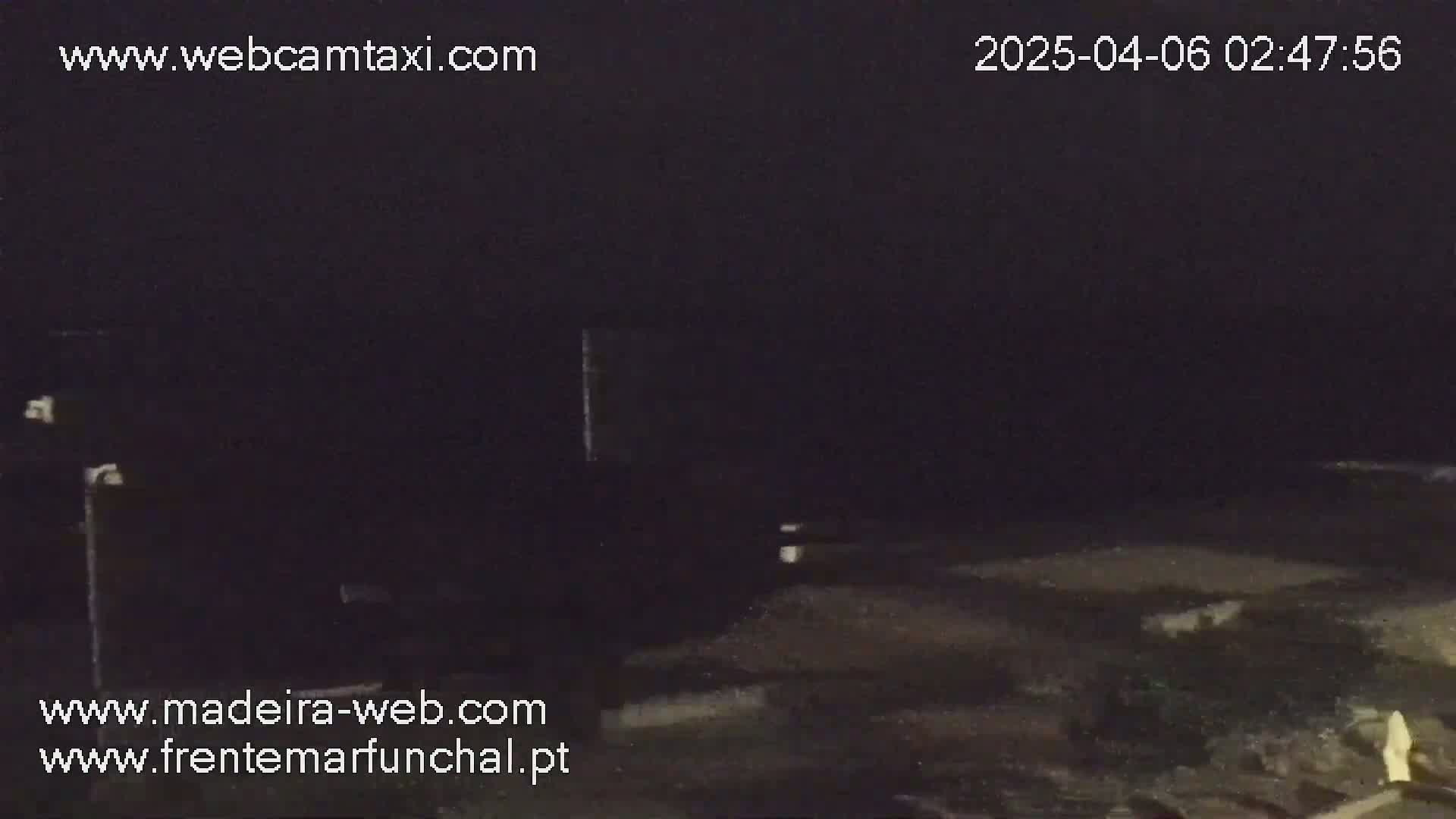 A dark, nighttime outdoor scene shows a mostly empty, dimly lit area with some indistinct objects in the distance.