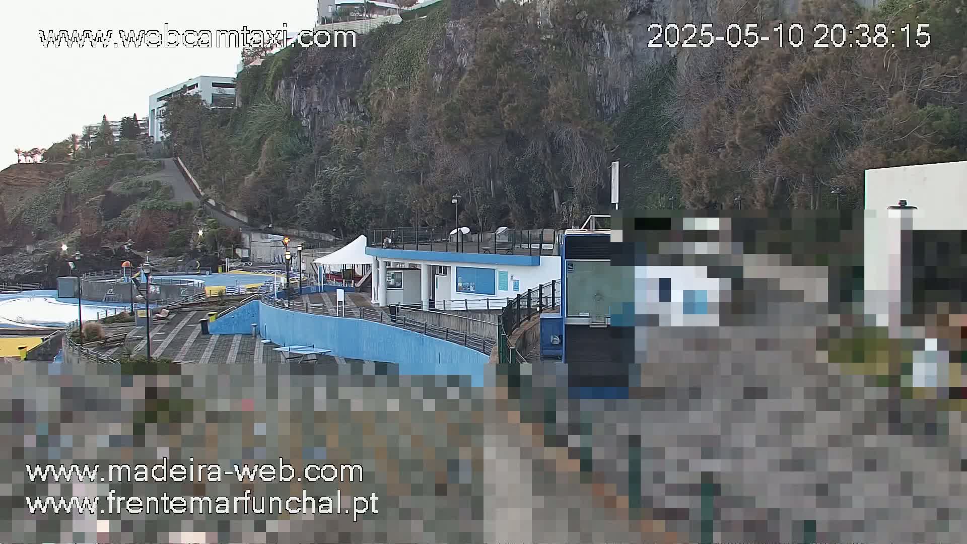 An outdoor view of a seaside complex with a pool area, a small building, and a cable car, situated on a cliffside under an overcast sky.