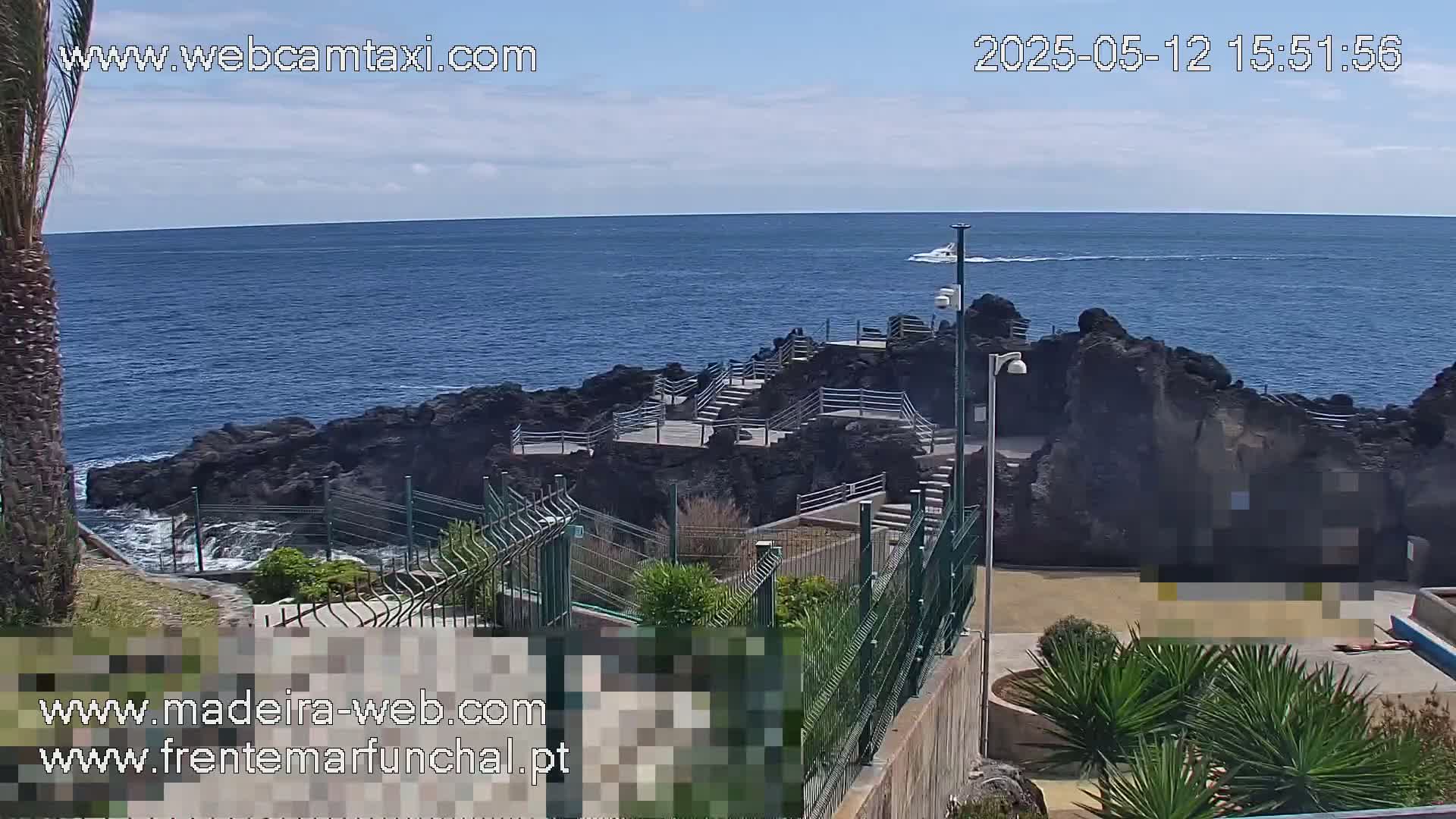 A rocky coastal area with stairs leading down to the ocean, under a partly cloudy sky, with a boat visible in the distance.
