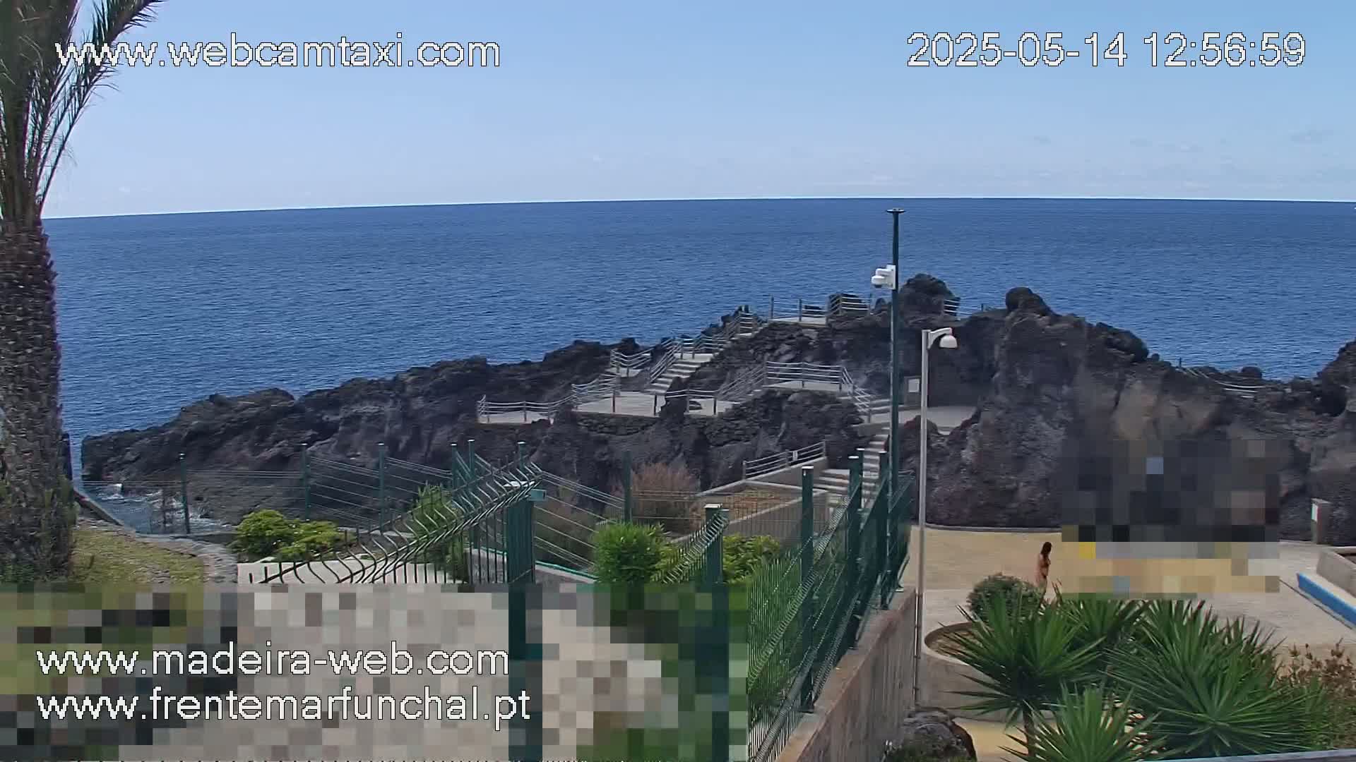 A rocky coastline with stairs leading down to the ocean, viewed from above on a sunny day.