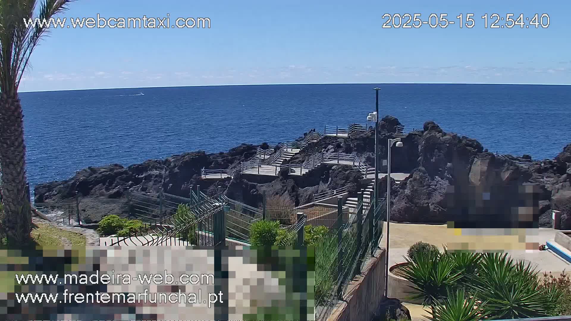 A rocky coastal area with stairs and railings leading down to the ocean, under a sunny sky.