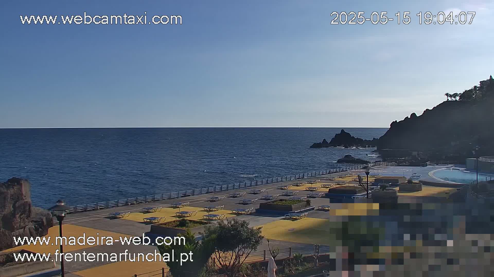 A clear, sunny day overlooks a calm ocean with a coastal area featuring an outdoor pool and lounge chairs.