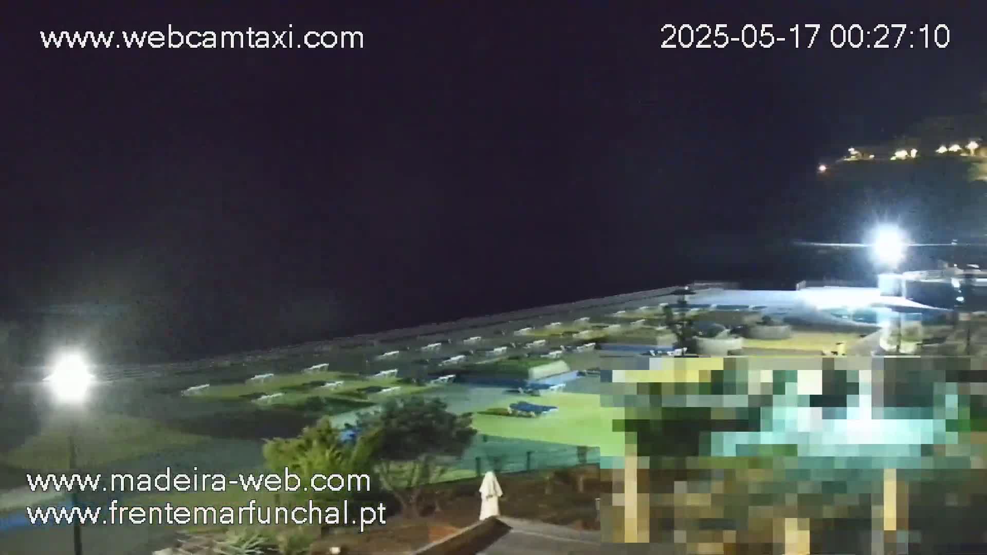 A nighttime view of a mostly empty waterfront area with some buildings and vegetation, under clear skies.