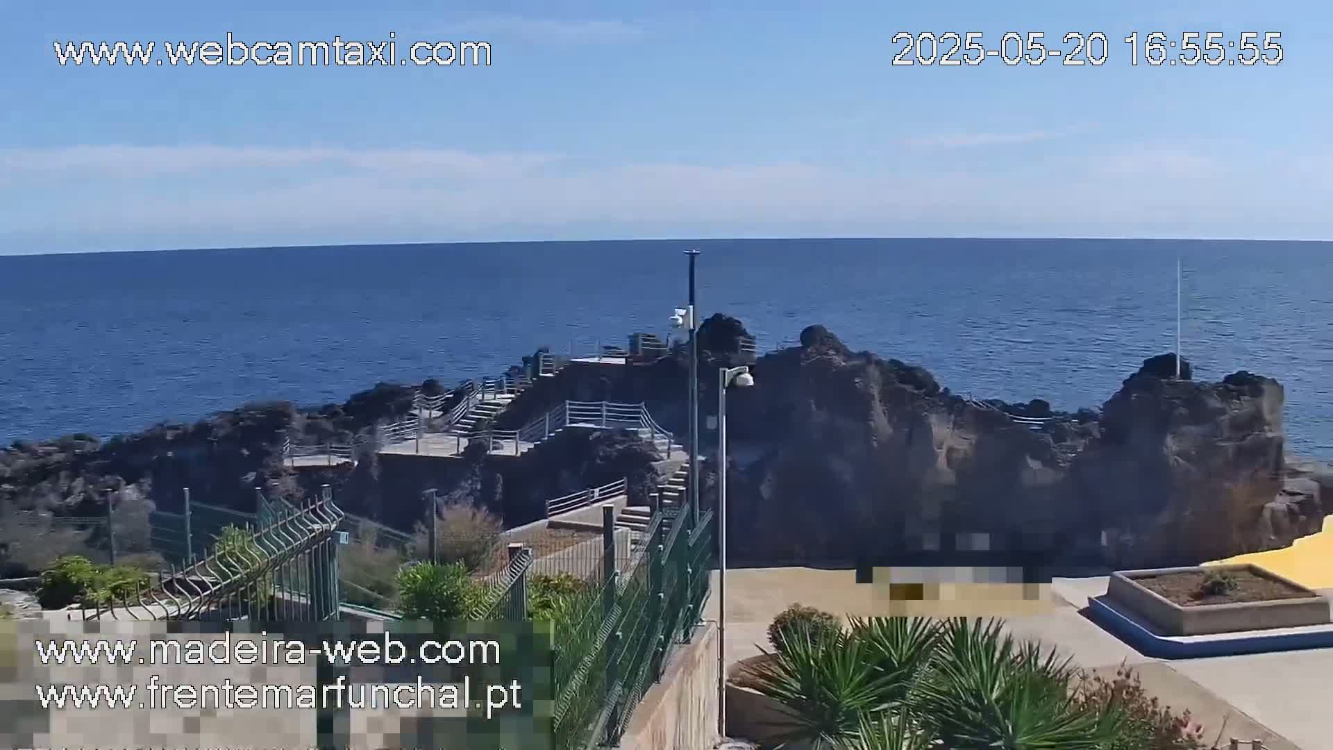 A rocky outcrop juts into a calm, blue ocean under a mostly sunny sky.
