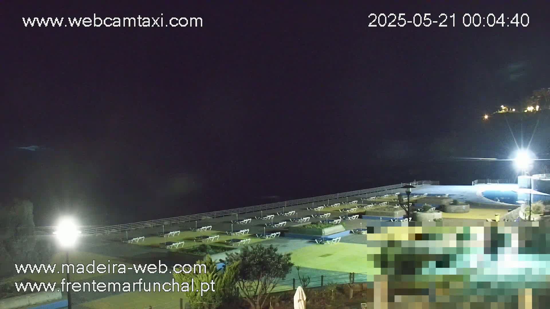 A nighttime view of an empty pool area with lounge chairs and a dark ocean in the background under a clear, dark sky.