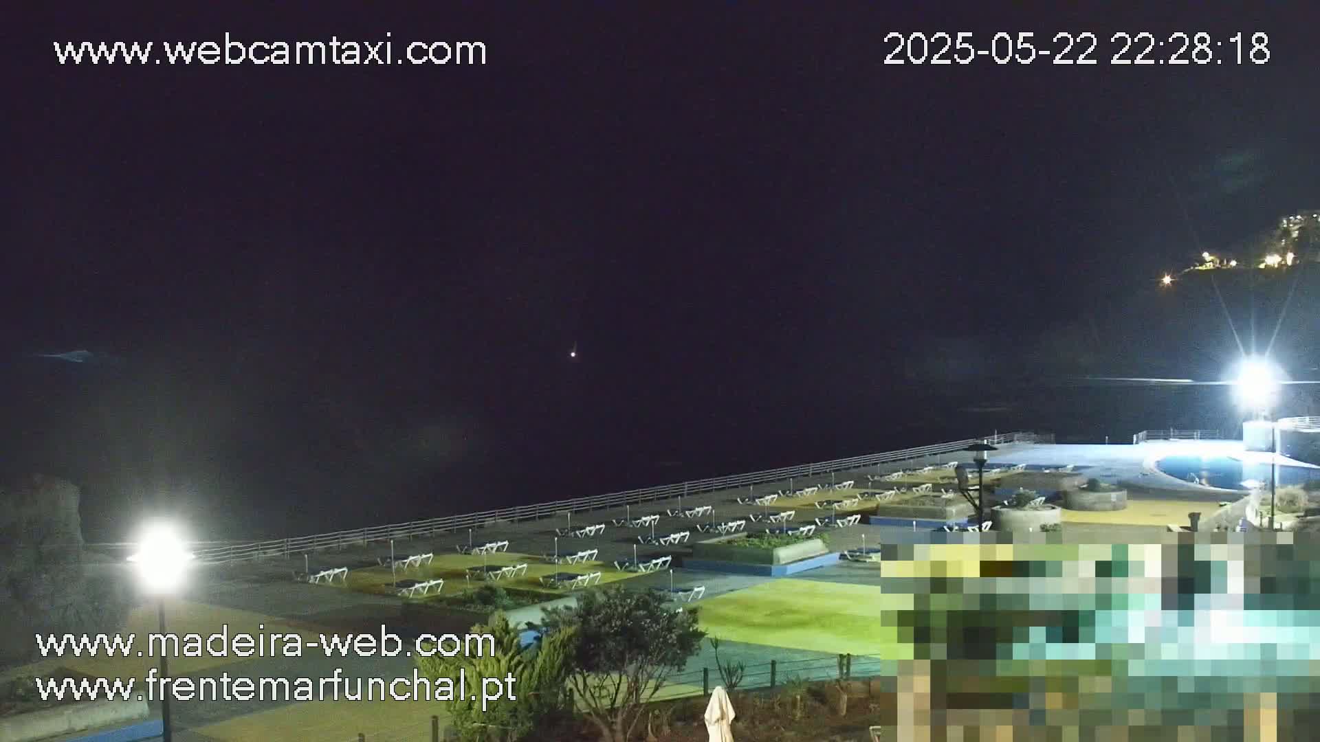 A nighttime view of an outdoor pool area with numerous lounge chairs and a dark ocean in the background under a clear, dark sky.