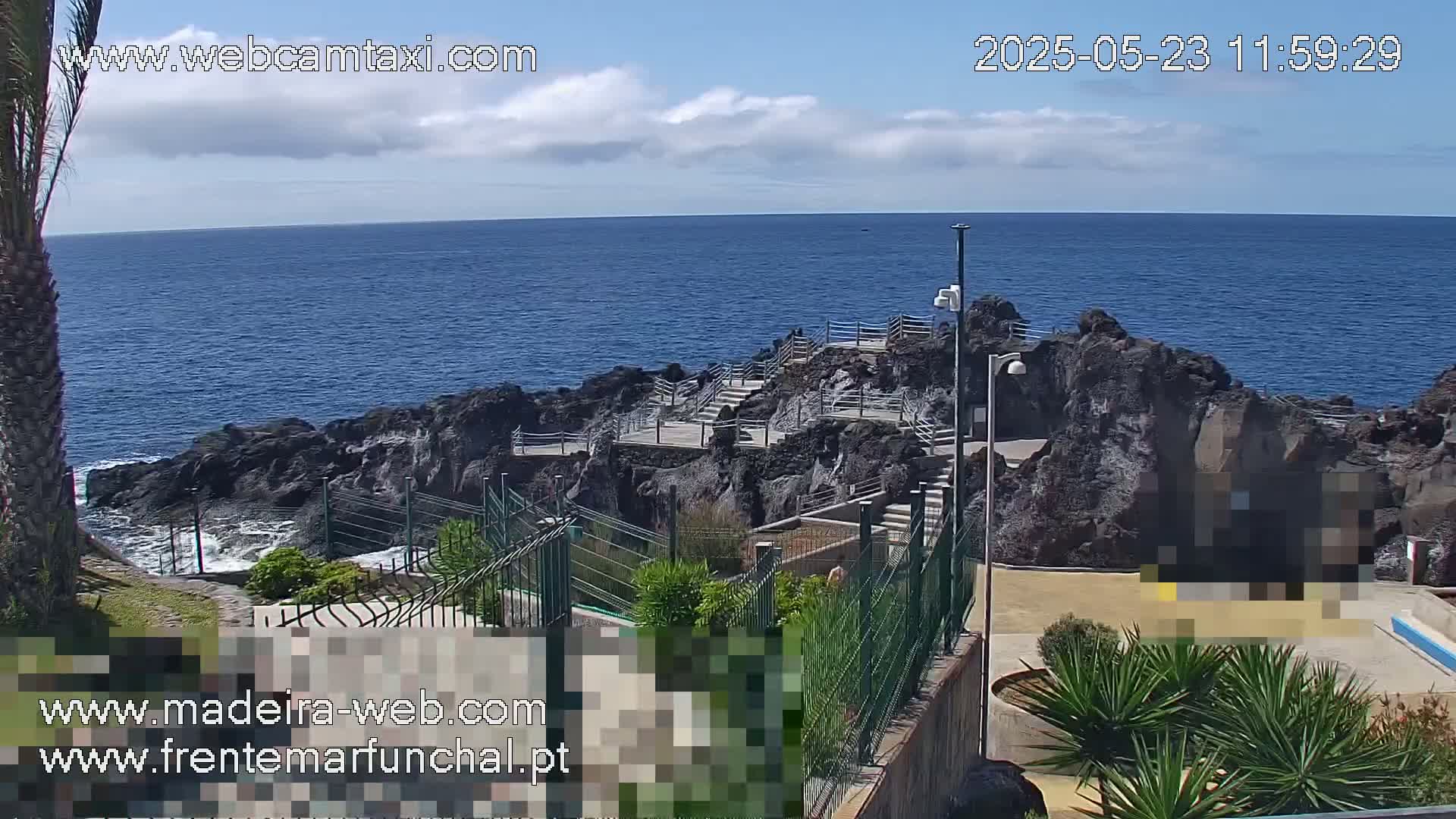 A rocky coastal area with stairs leading down to the ocean, under partly cloudy skies.