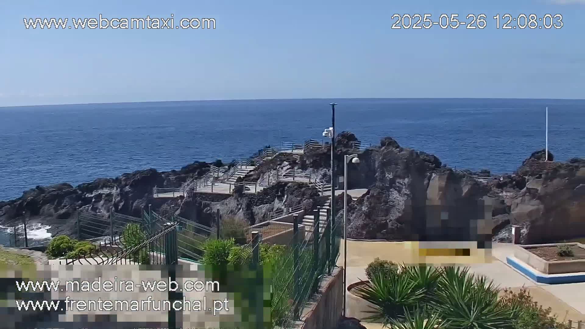A rocky coastal area with stairs leading down to the ocean under a clear, sunny sky.