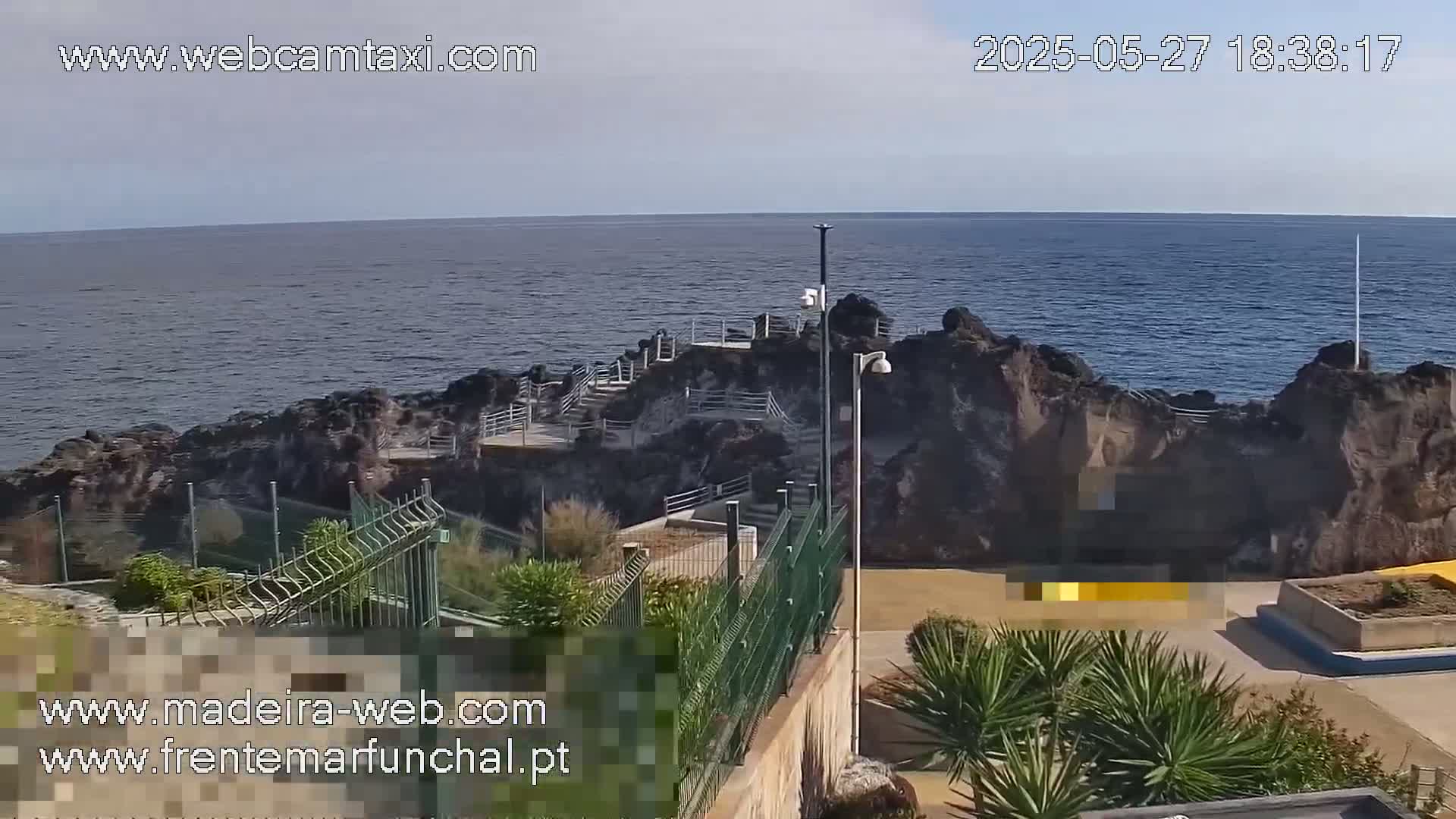 A rocky coastline with stairs leading down to the ocean is visible under a clear sky.