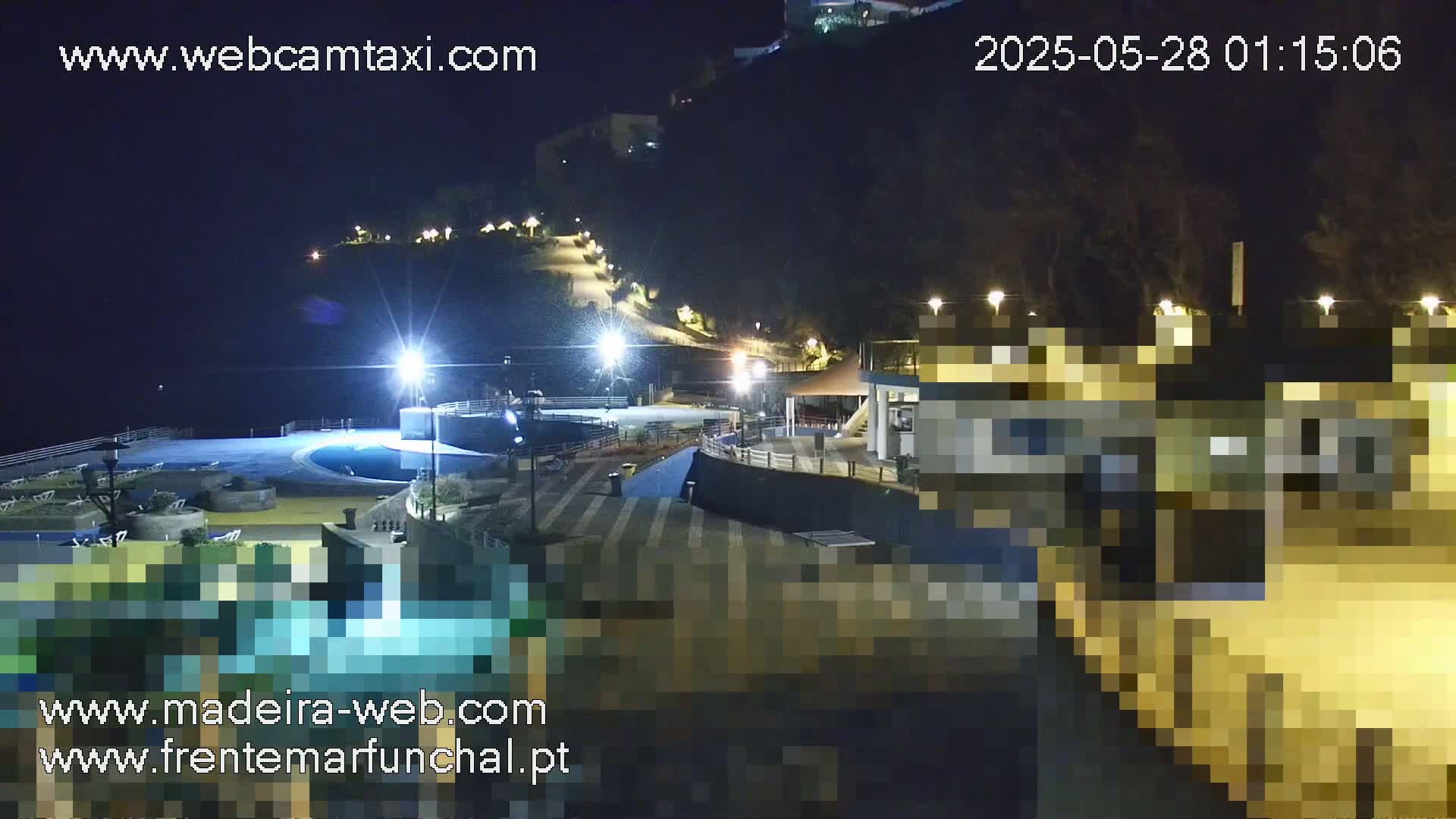 A nighttime view of a resort area with a pool, buildings, and a sloped pathway leading up a hill.