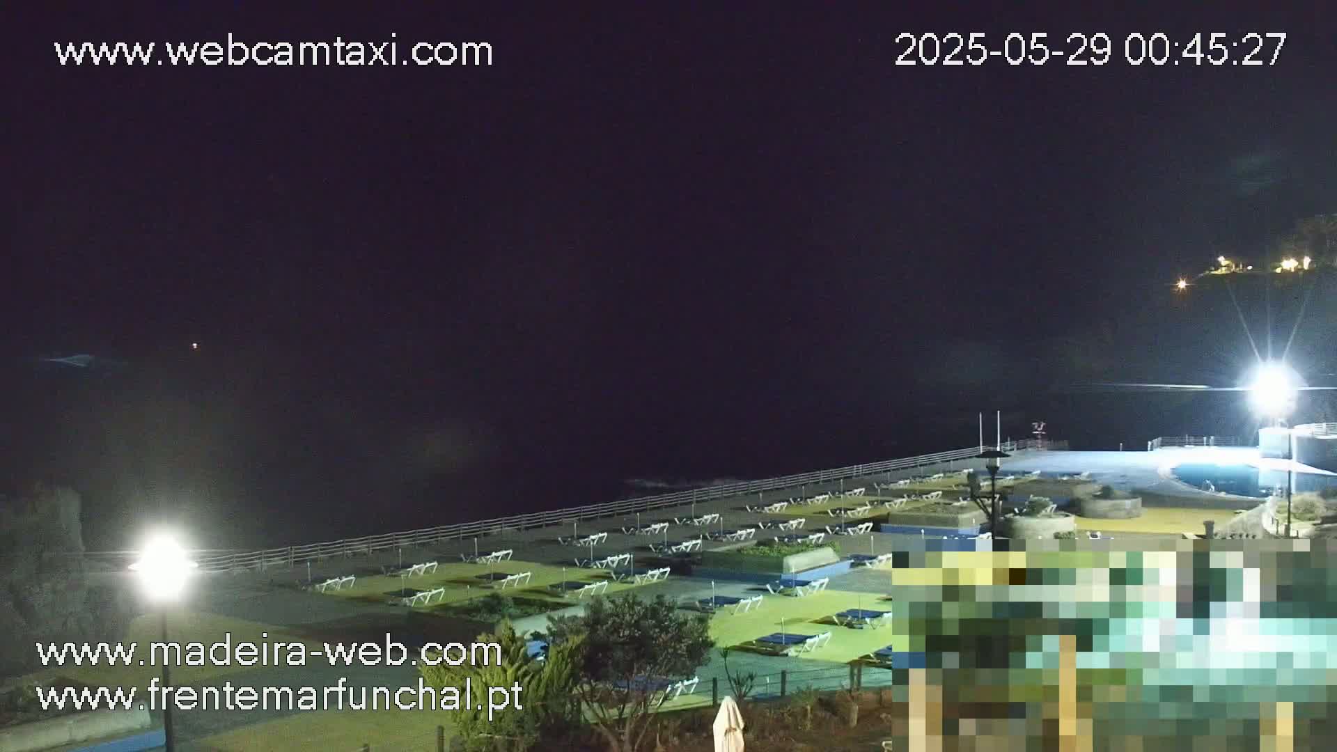 A nighttime view of an empty outdoor pool area with rows of lounge chairs next to the ocean under a clear, dark sky.