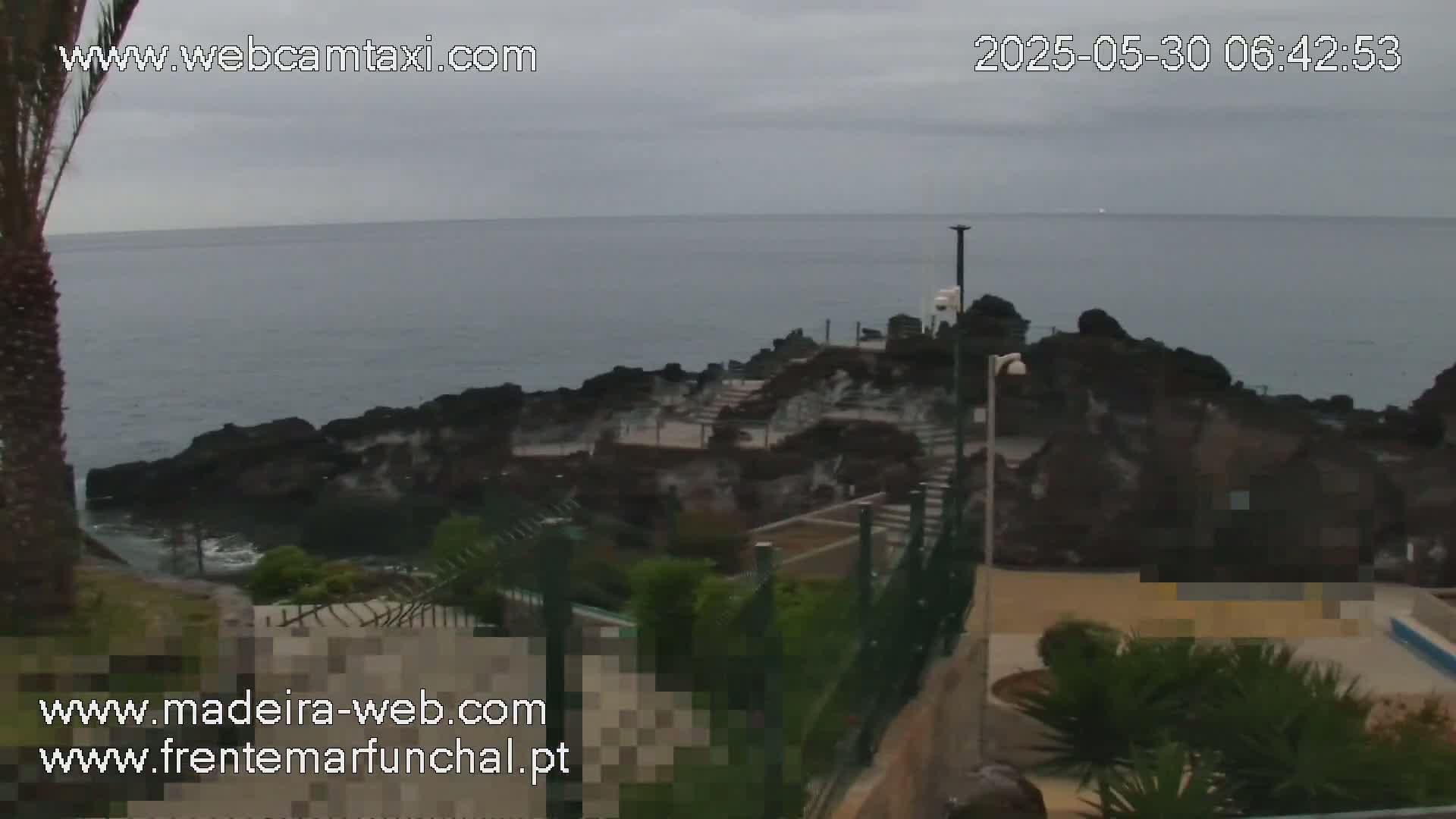 A rocky coastline with steps leading down to the ocean is visible under an overcast sky.