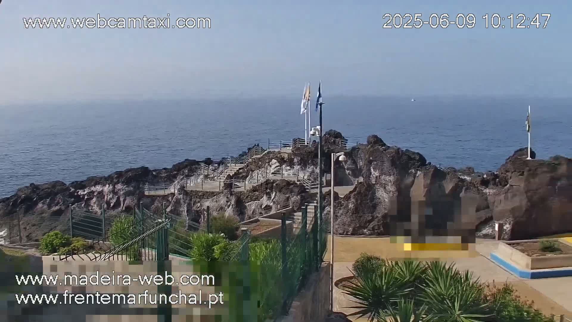 A rocky outcrop on a coast juts into a calm ocean under a hazy sky.