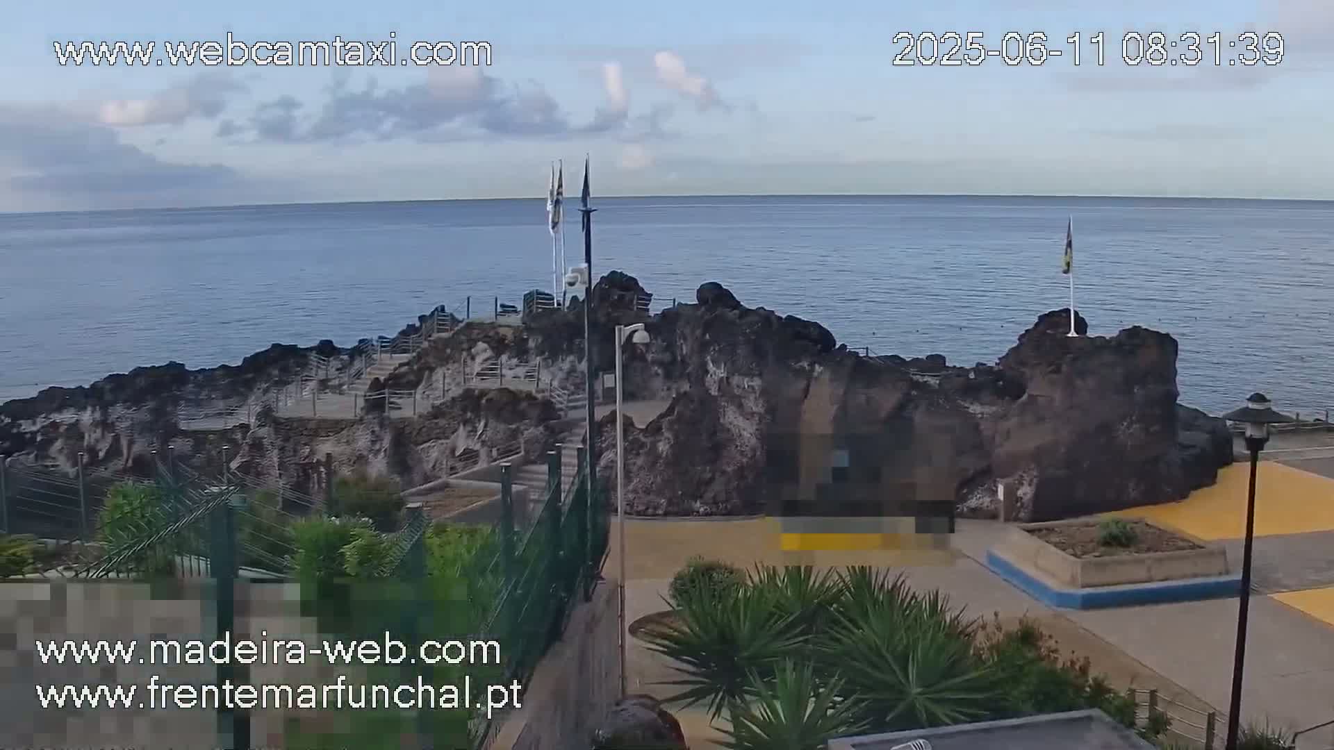 A rocky outcrop juts into a calm ocean under a mostly clear sky.