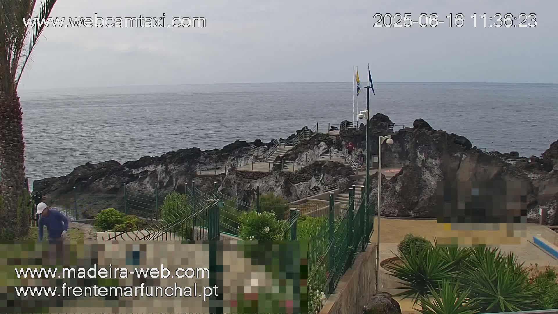 A rocky coastline with stairs leading down to the ocean, under an overcast sky, is partially fenced and has some landscaping.