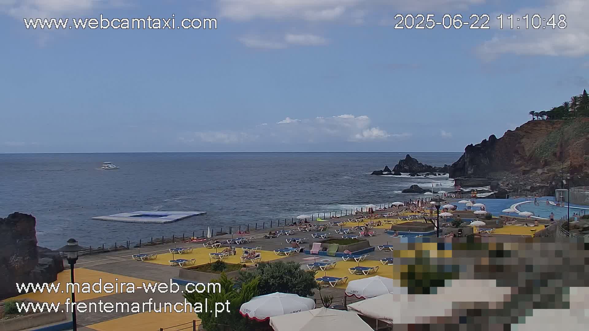 An outdoor oceanside swimming complex with a partly cloudy sky and many people relaxing on lounge chairs.