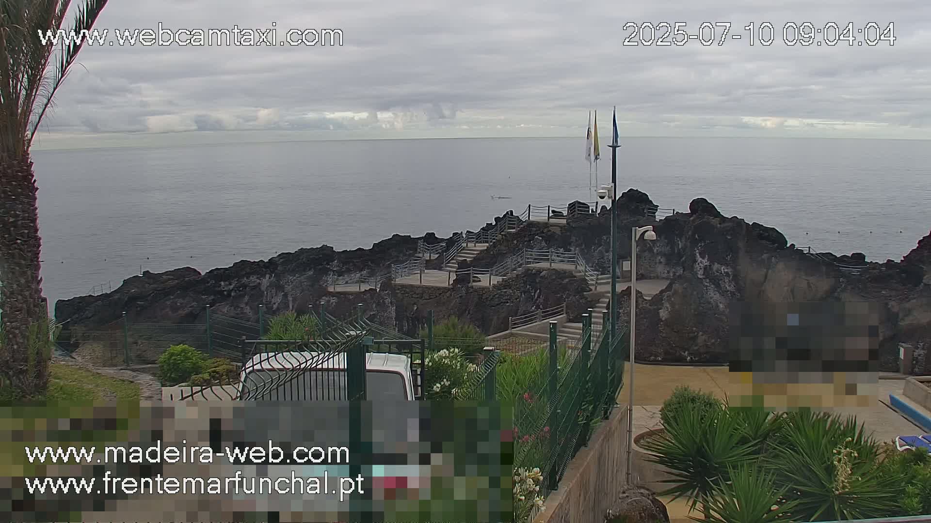 A rocky coastline overlooks a calm ocean under a cloudy sky, with stairs leading down to the water's edge.