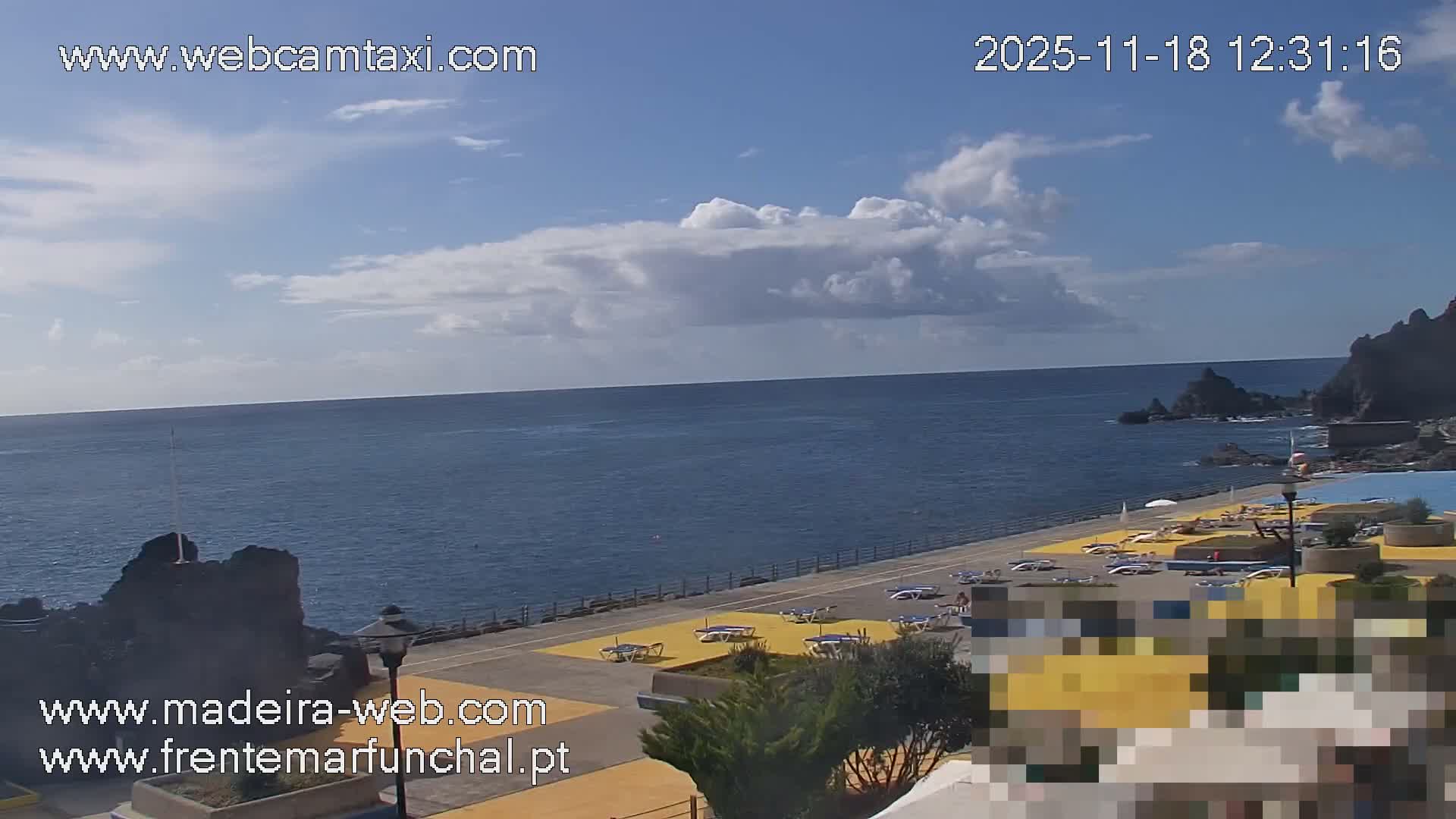 A nighttime view shows a dark, rocky coastline with a beach area containing lounge chairs, illuminated by a lamppost, under a mostly clear, dark sky.