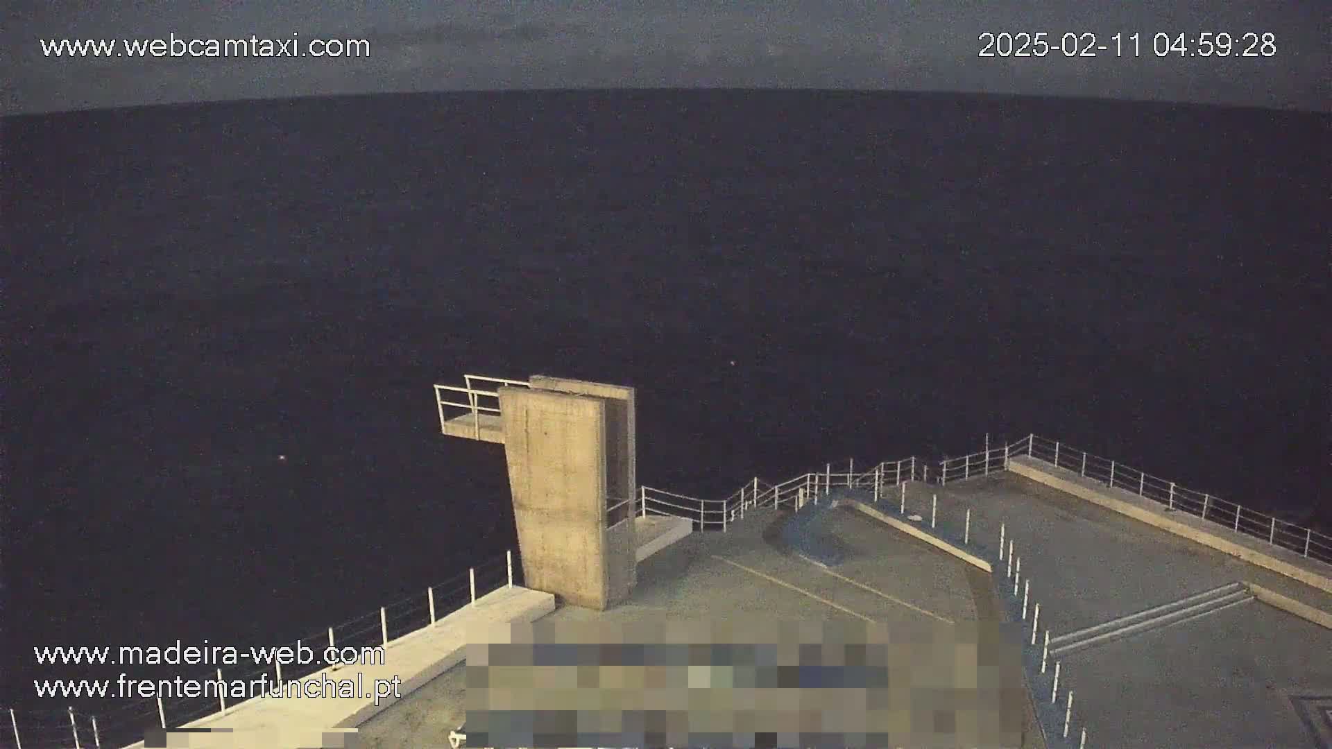 A high-angle, nighttime view shows a concrete diving platform overlooking a dark body of water under a dark, overcast sky.