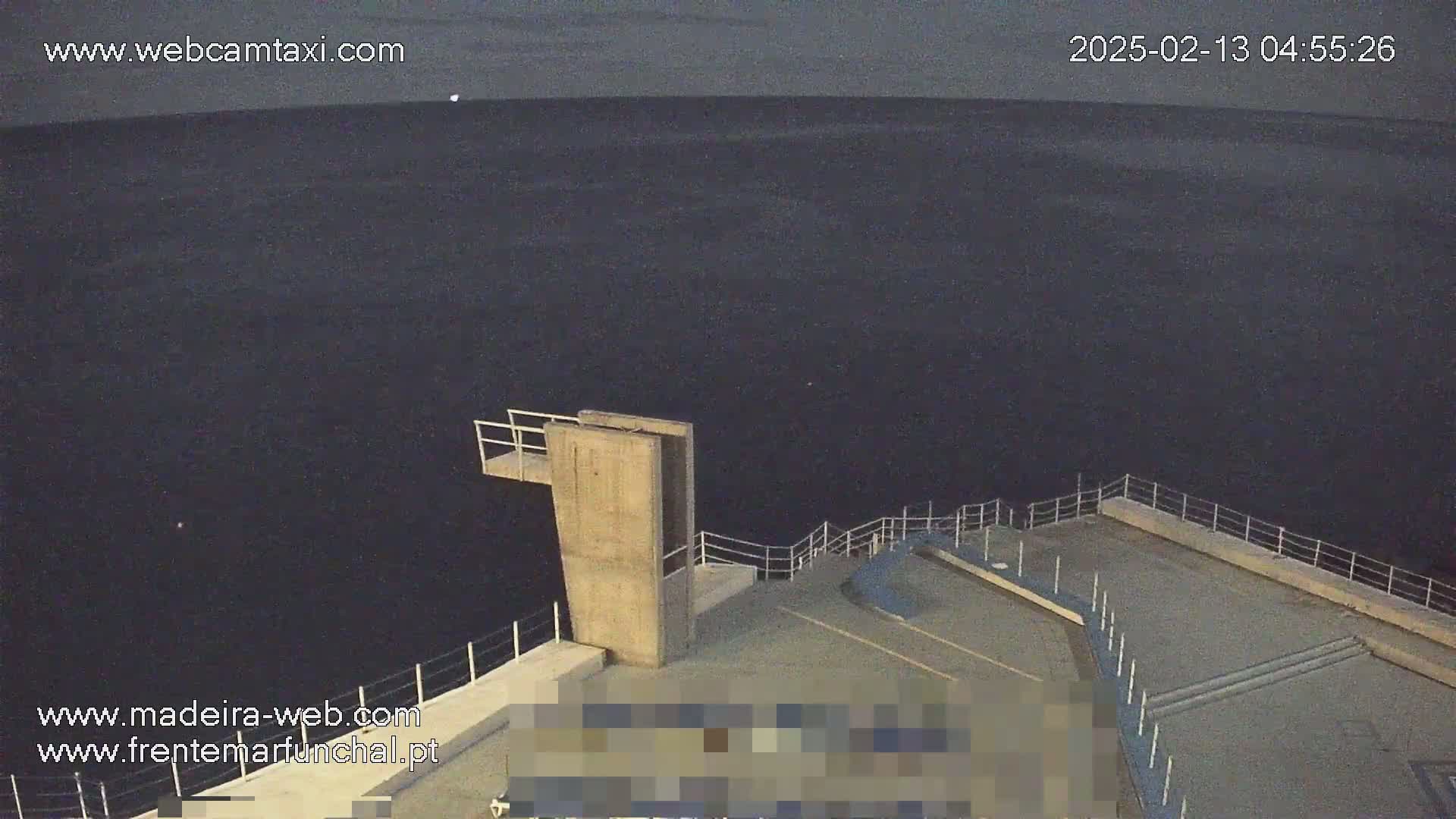 A high-angle, nighttime view shows a concrete diving platform overlooking dark water under a mostly clear, dusky sky.