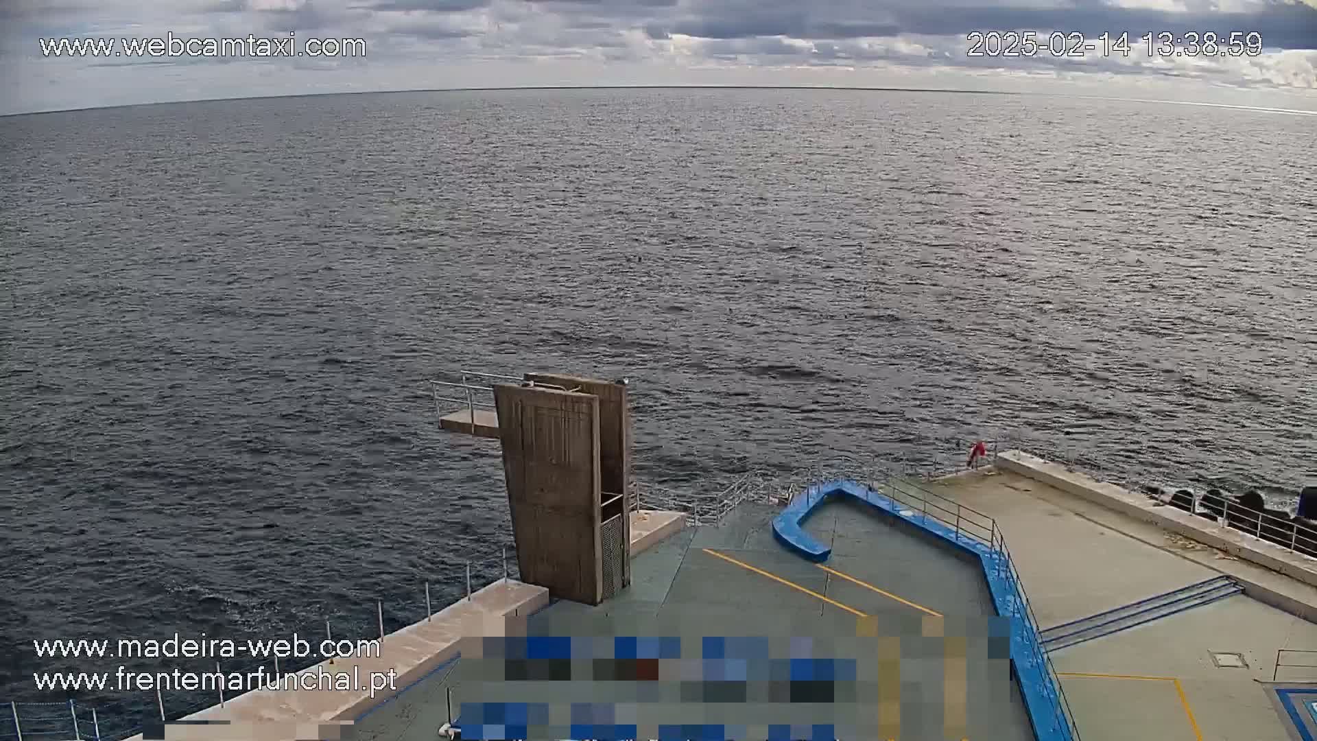 A mostly cloudy day shows a view of a body of water with a diving platform and a paved area next to it.