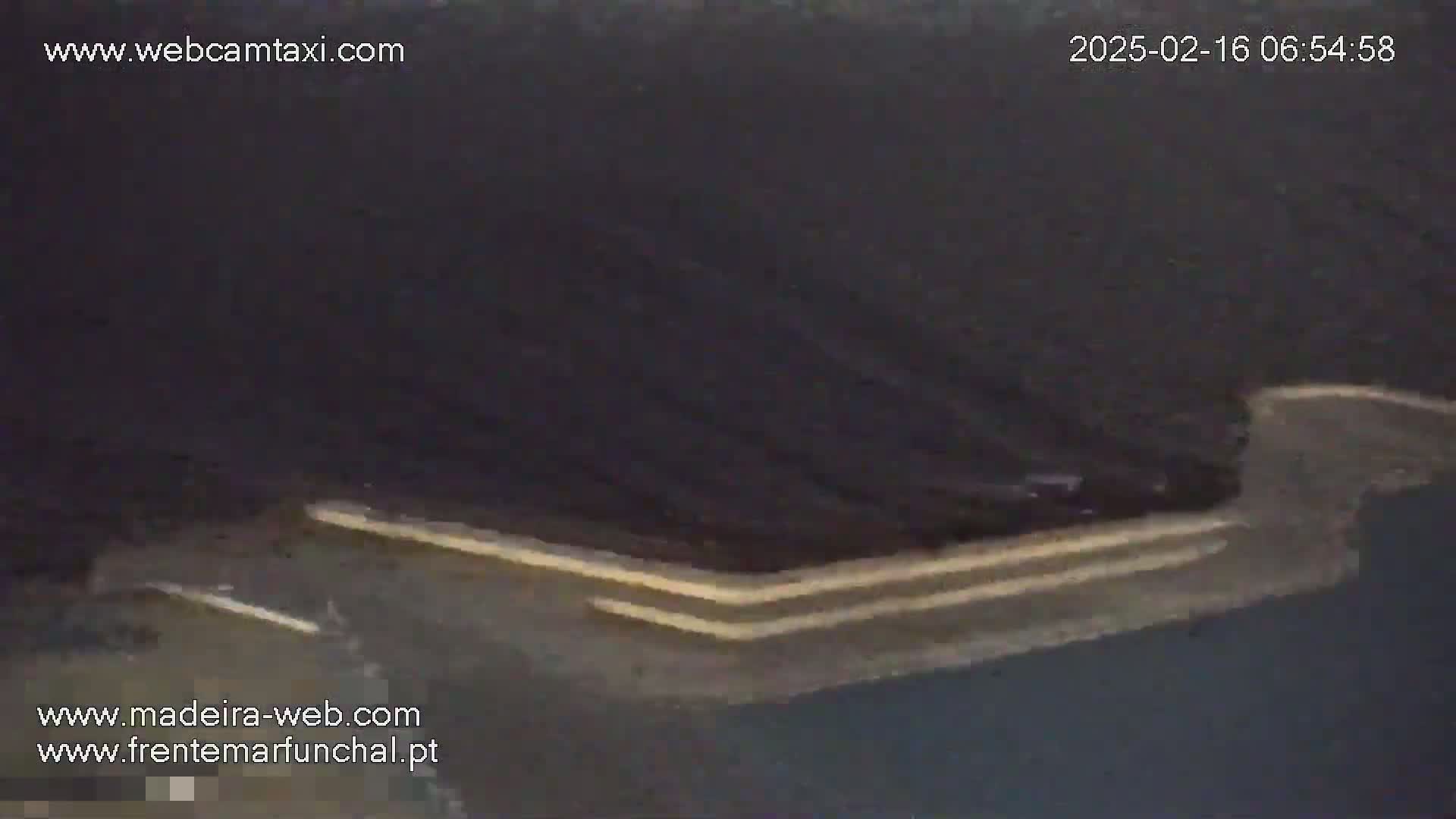 A dark, possibly nighttime, aerial view shows a curving road with pale lane markings.