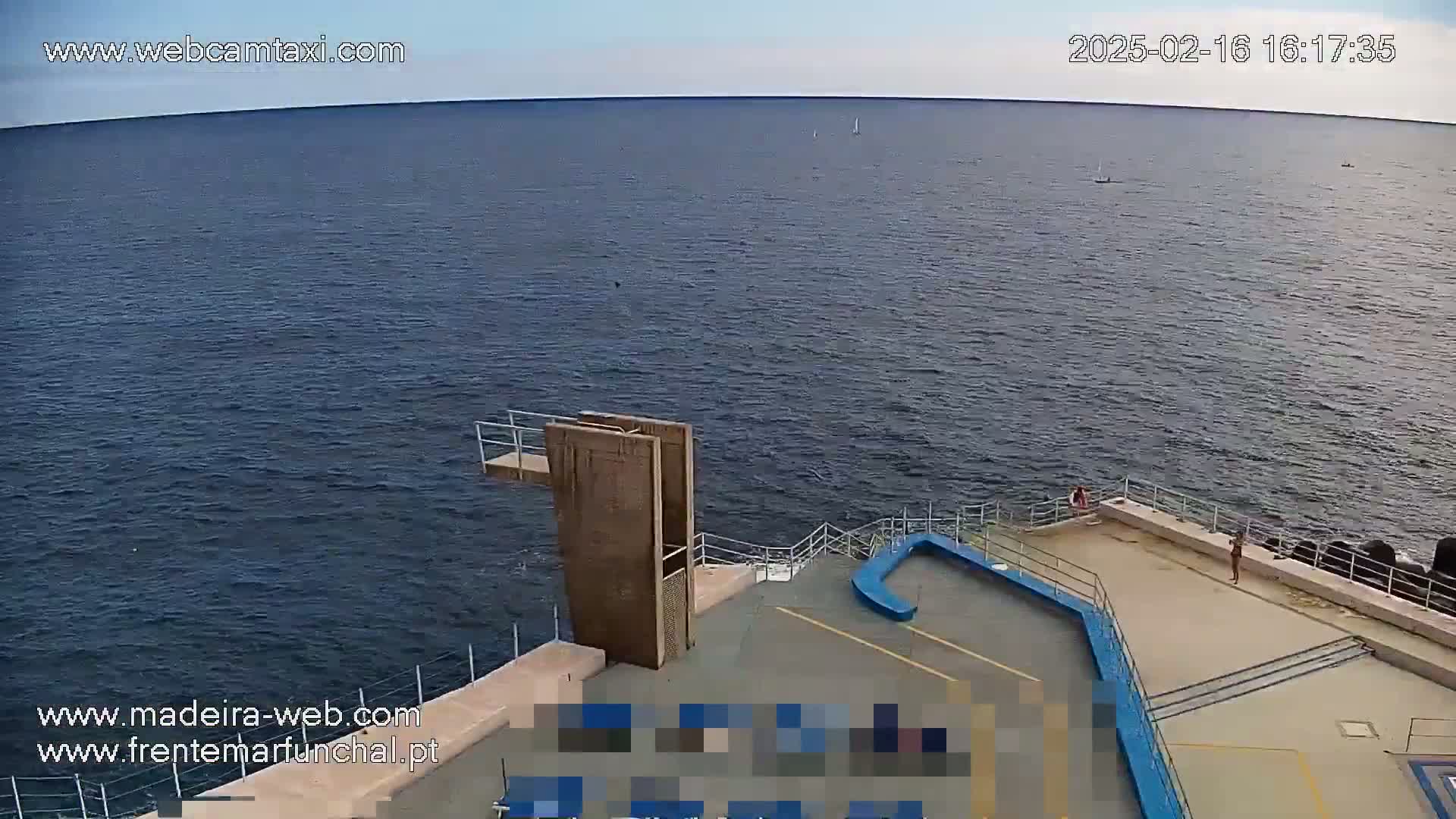 A diving platform overlooks a calm, dark-blue ocean on a mostly clear day.