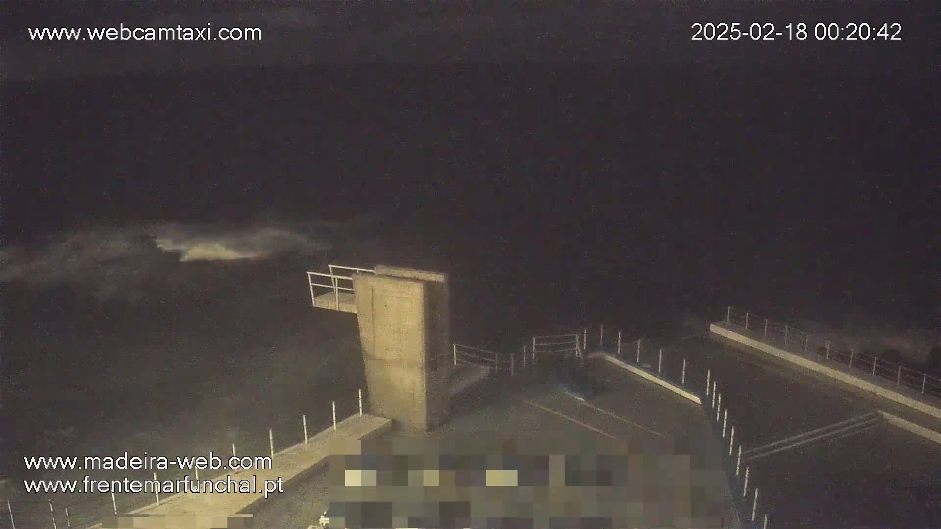 A nighttime view of a concrete structure near a body of water with slightly choppy waves under a dark sky.