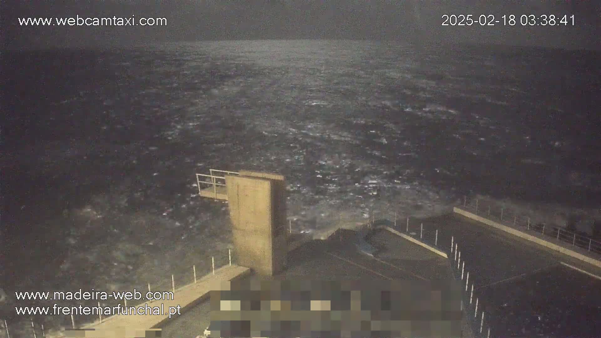 A nighttime view of rough, dark water crashing against a concrete structure.