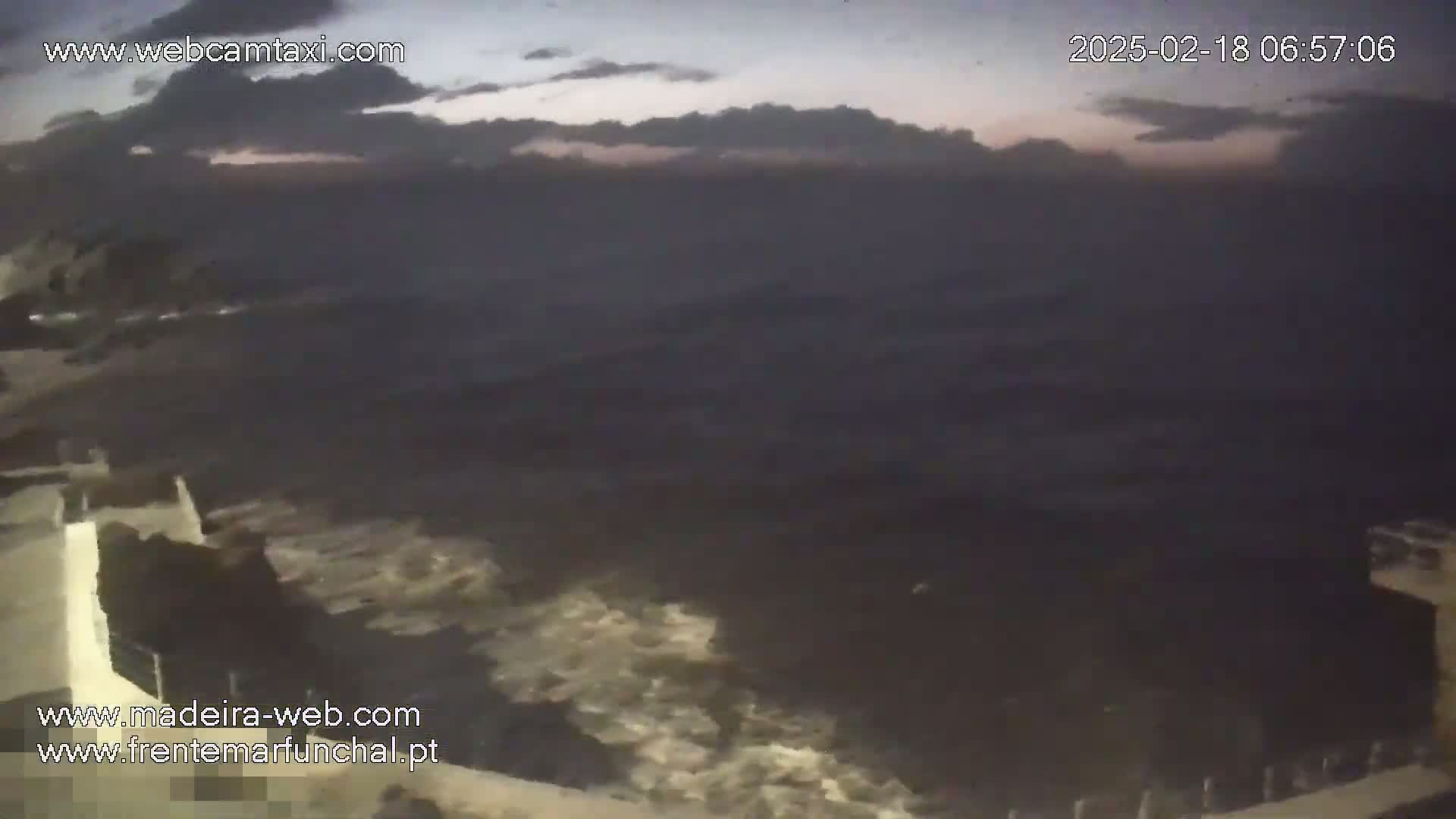 A dark, overcast sky hangs over a rough, dark sea meeting a low, light-colored wall.